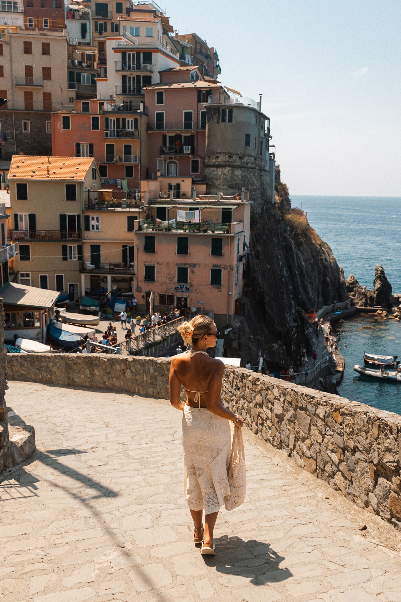 Woman walking down stone path overlooking colorful houses in Manarola, Cinque Terre, Italy.