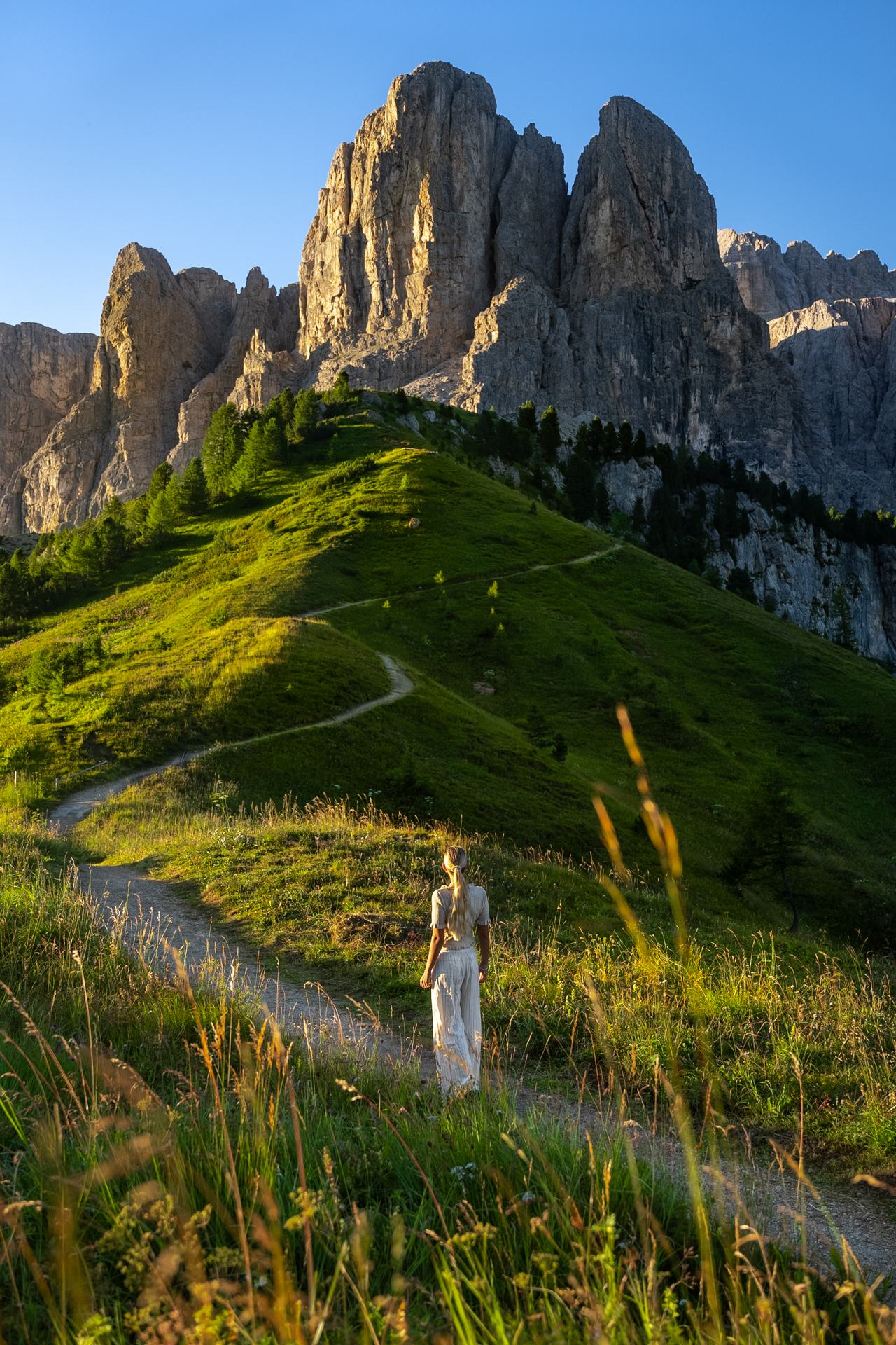 Woman walking on mountain trail surrounded by golden light in the Dolomites, Italy.