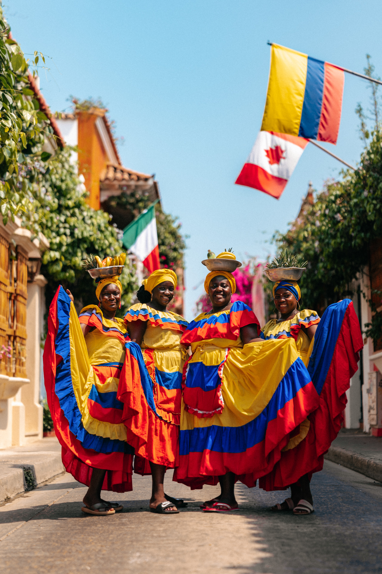 Group of Afro-Colombian women in traditional colorful dresses posing with fruit baskets on their heads in Cartagena, Colombia.