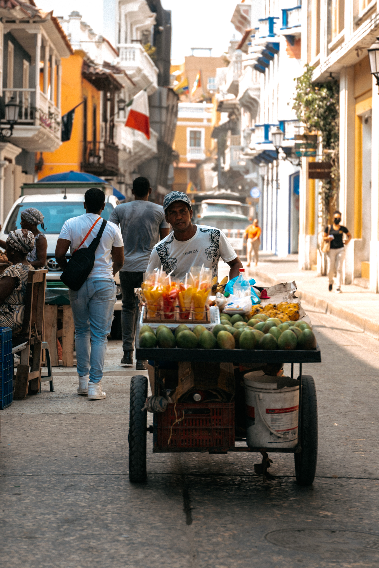 Street vendor pushing a fruit cart through the colorful colonial streets of Cartagena, Colombia.