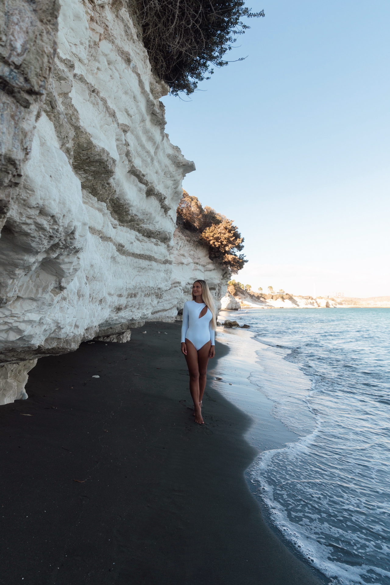 Woman in white swimsuit walking along dramatic white cliffs at Governor’s Beach, Cyprus.