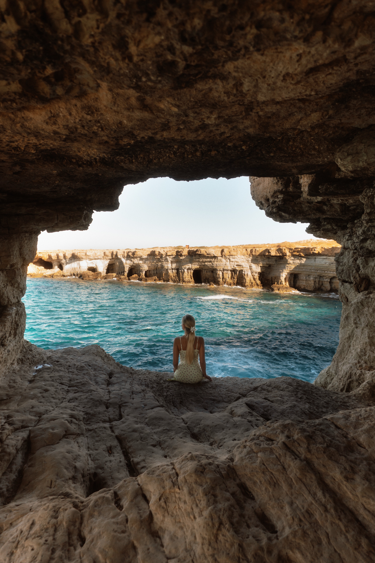 Woman sitting inside a sea cave overlooking turquoise waters at Cape Greco, Cyprus.