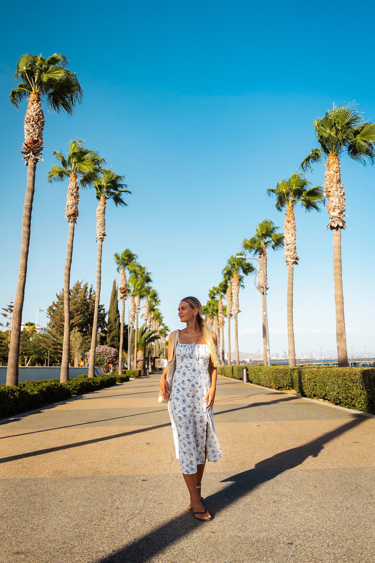 Woman walking along palm-lined promenade at Molos Park in Limassol, Cyprus, on a sunny day.