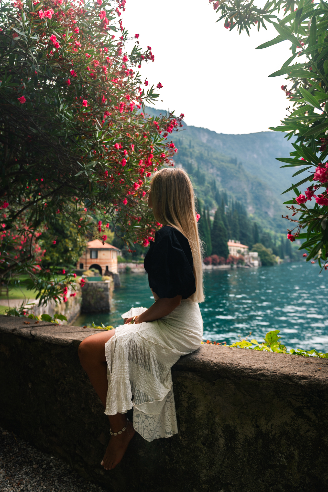 Traveler sitting by blooming flowers, overlooking the serene waters and villas of Lake Como, Italy