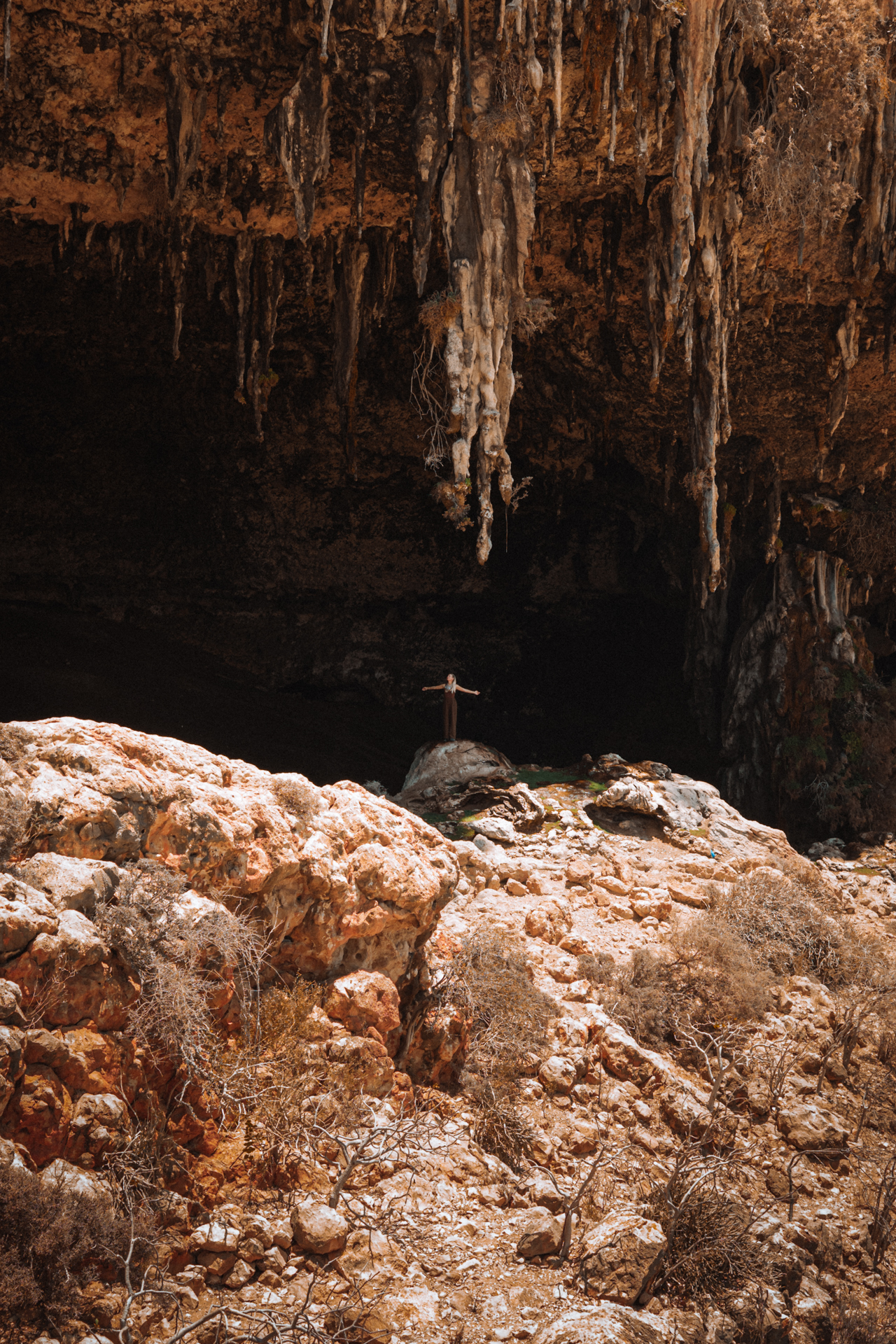Traveler standing inside Dagub cave with stalactites in Socotra’s rocky terrain.
