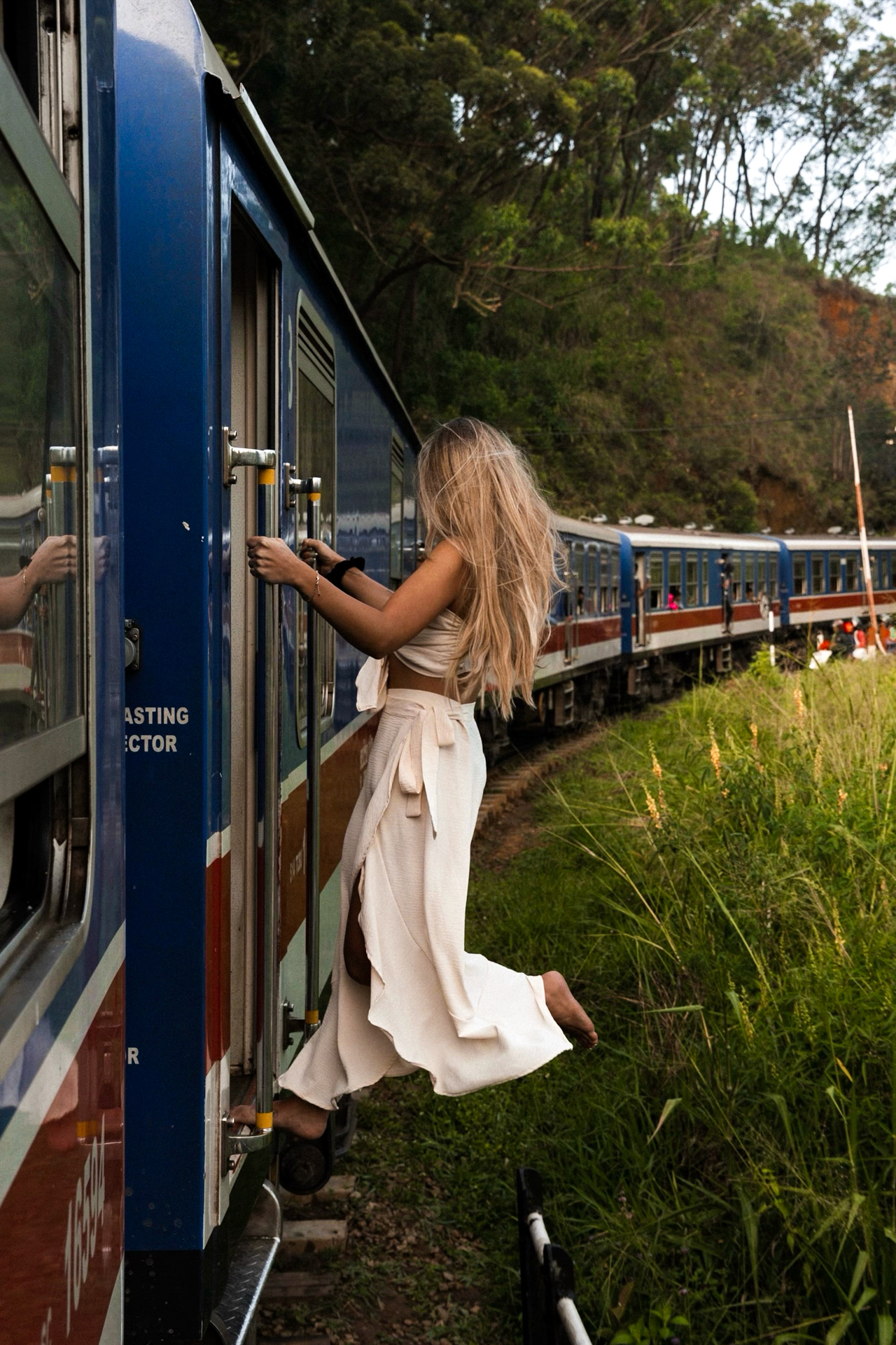 Sri Lanka Train Ride – Traveler hanging onto the famous blue train in Sri Lanka, surrounded by lush greenery.