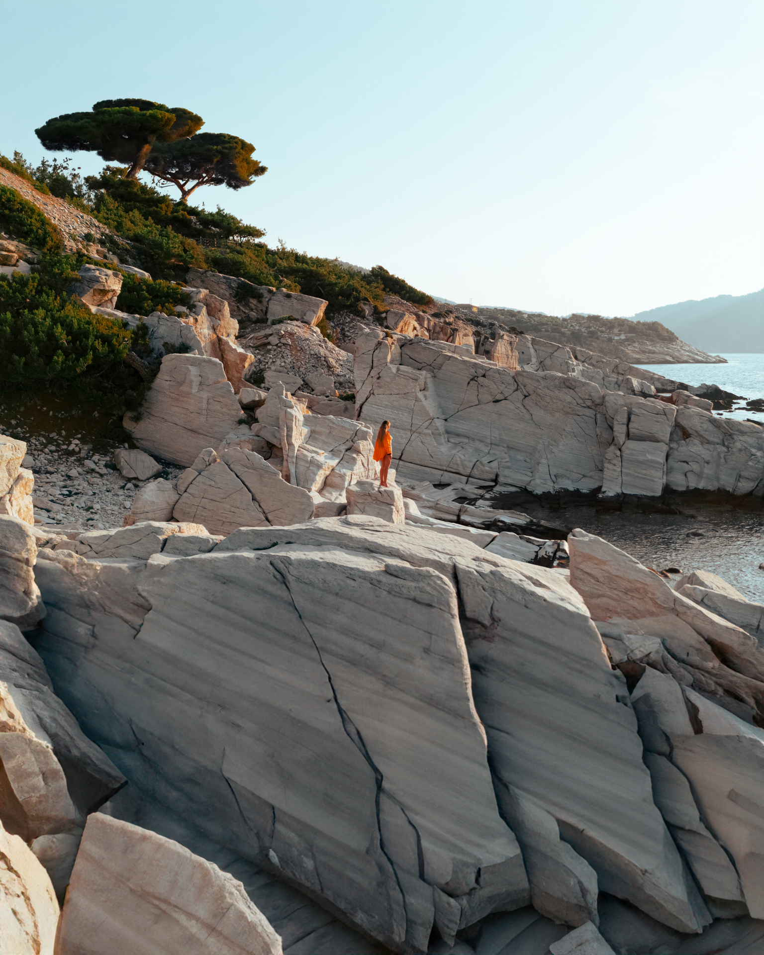 Thassos Woman in orange dress standing on rocky cliffs by the sea in Thassos, Greece.