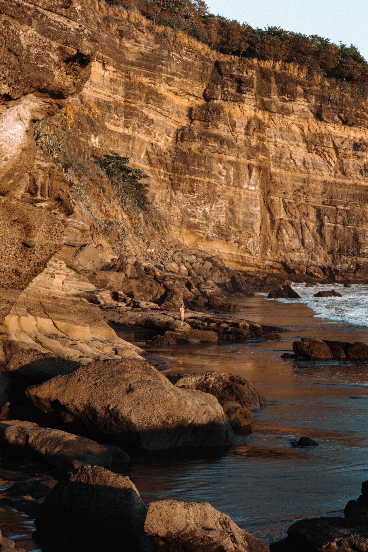 El Zonte Traveler standing on coastal rocks below golden cliffs at sunset in El Salvador.
