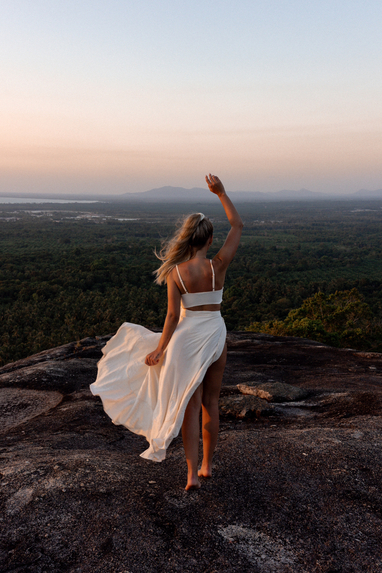 Woman on Batu Baginda, a granite rock at sunset overlooking Belitung jungle landscape