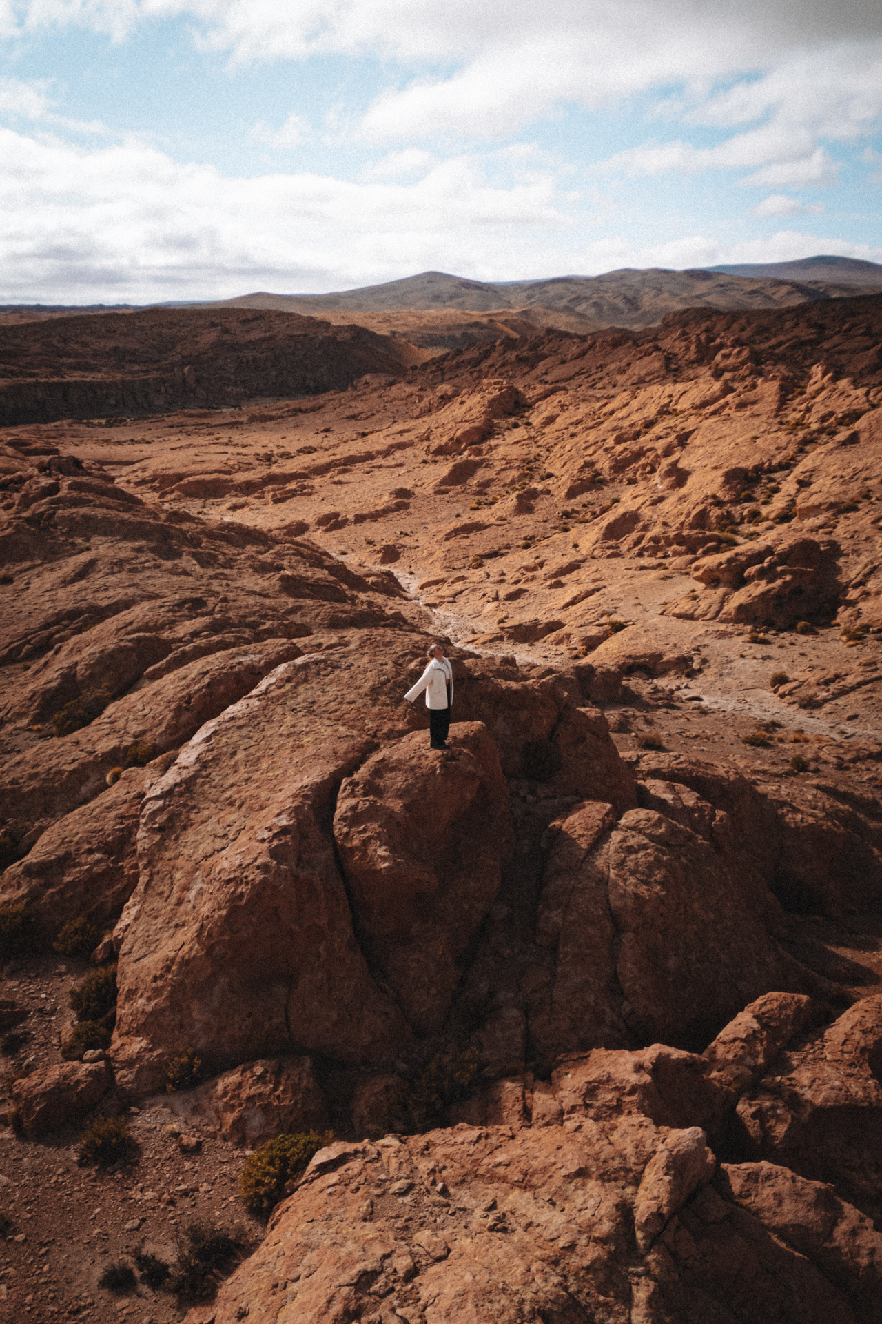 Traveler standing on reddish rock formations surrounded by rugged desert terrain in Siloli Desert, Bolivia.