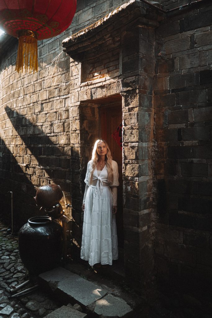 China Woman in white dress at traditional Fujian stone building, China