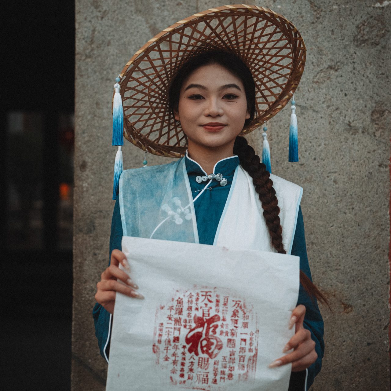 Culture in China Woman wearing traditional Chinese attire and bamboo hat holding a red printed paper at a heritage site in Fujian, China