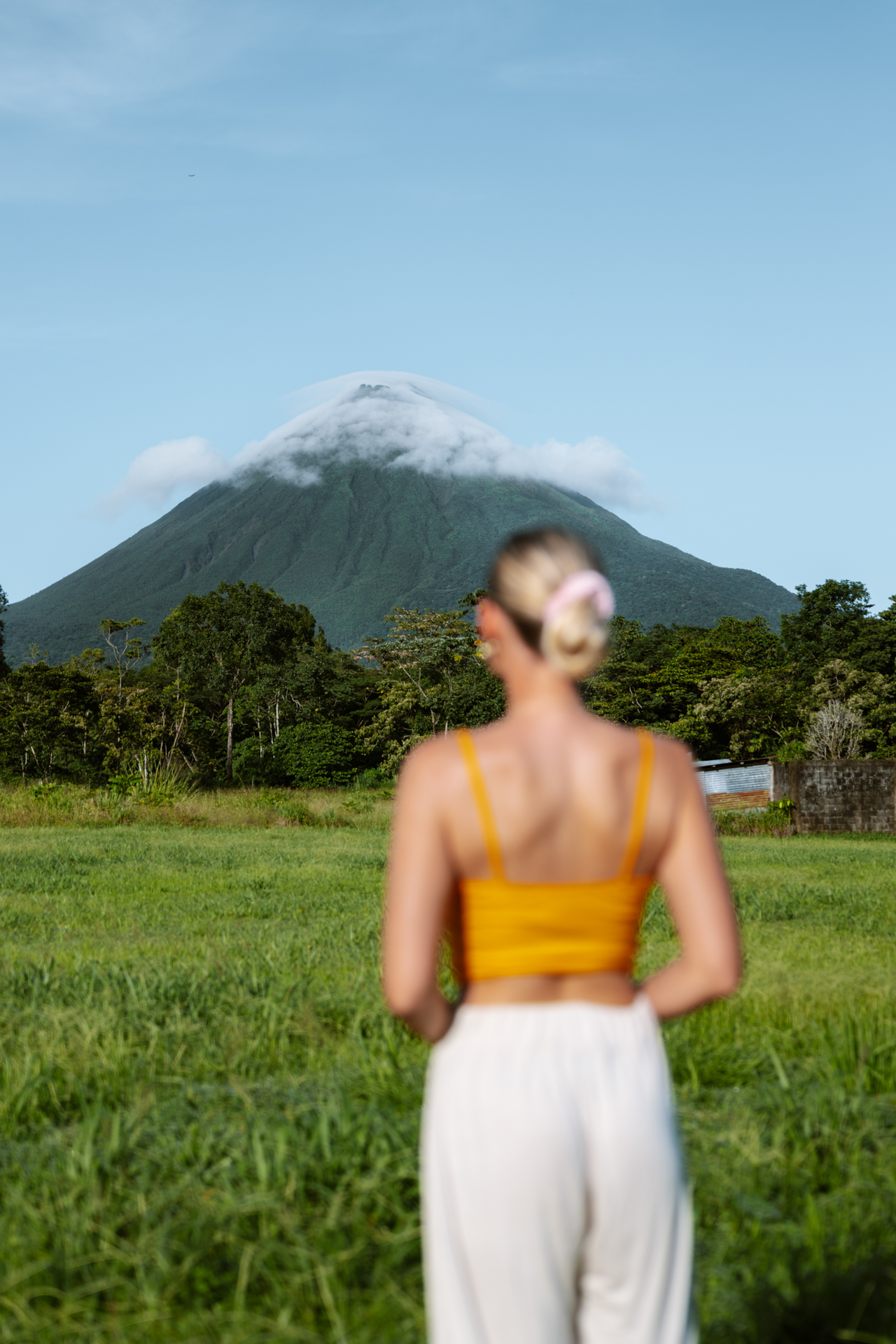 Woman standing in a green field facing Arenal Volcano near La Fortuna, Costa Rica