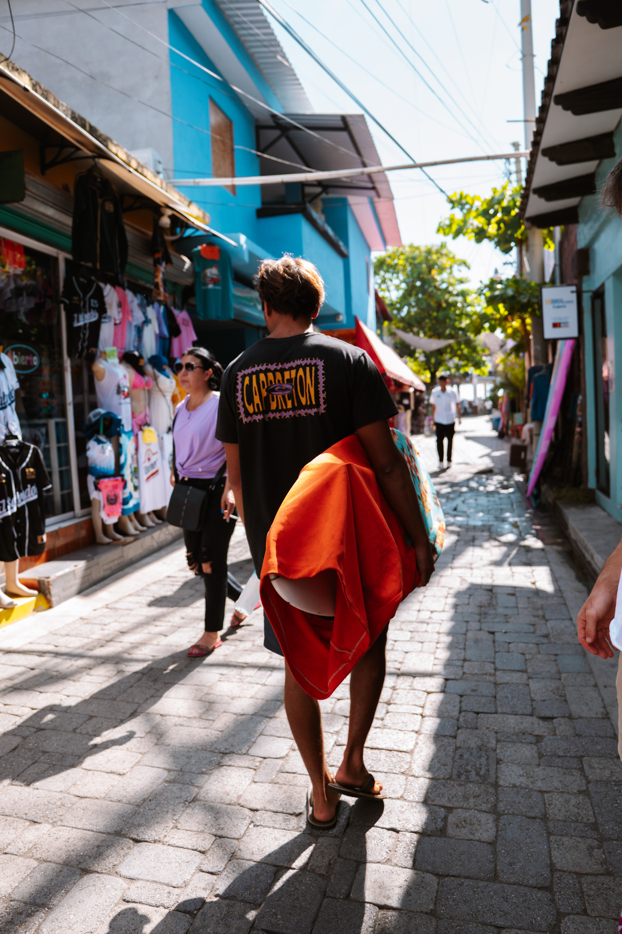Surfer walking through El Tunco street with board at sunny seaside town