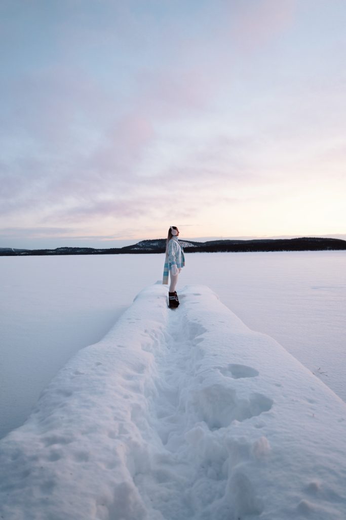 Inari Person standing on a snowy pier overlooking a frozen lake at sunset in Saariselkä, Finland