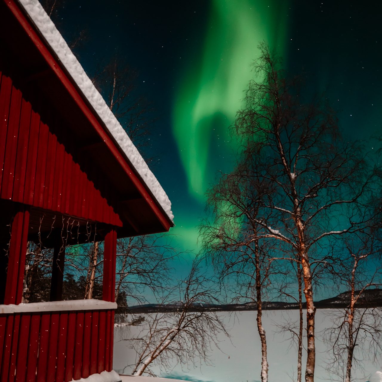 Traditions in Finland Northern lights over red cabin and frozen lake in Finnish Lapland