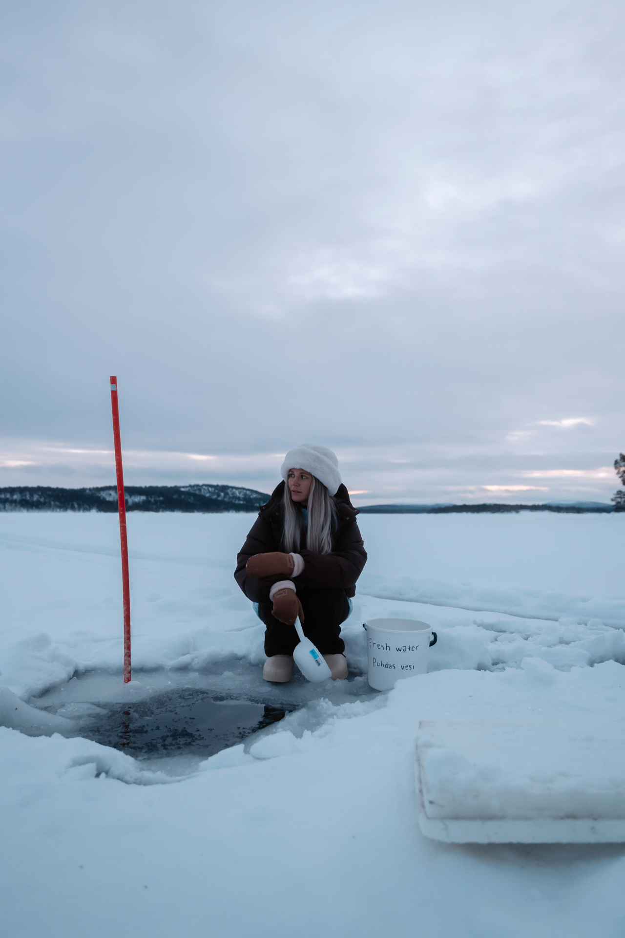 Inari Woman collecting fresh water from a hole in a frozen lake surrounded by snow in Inari, Finland