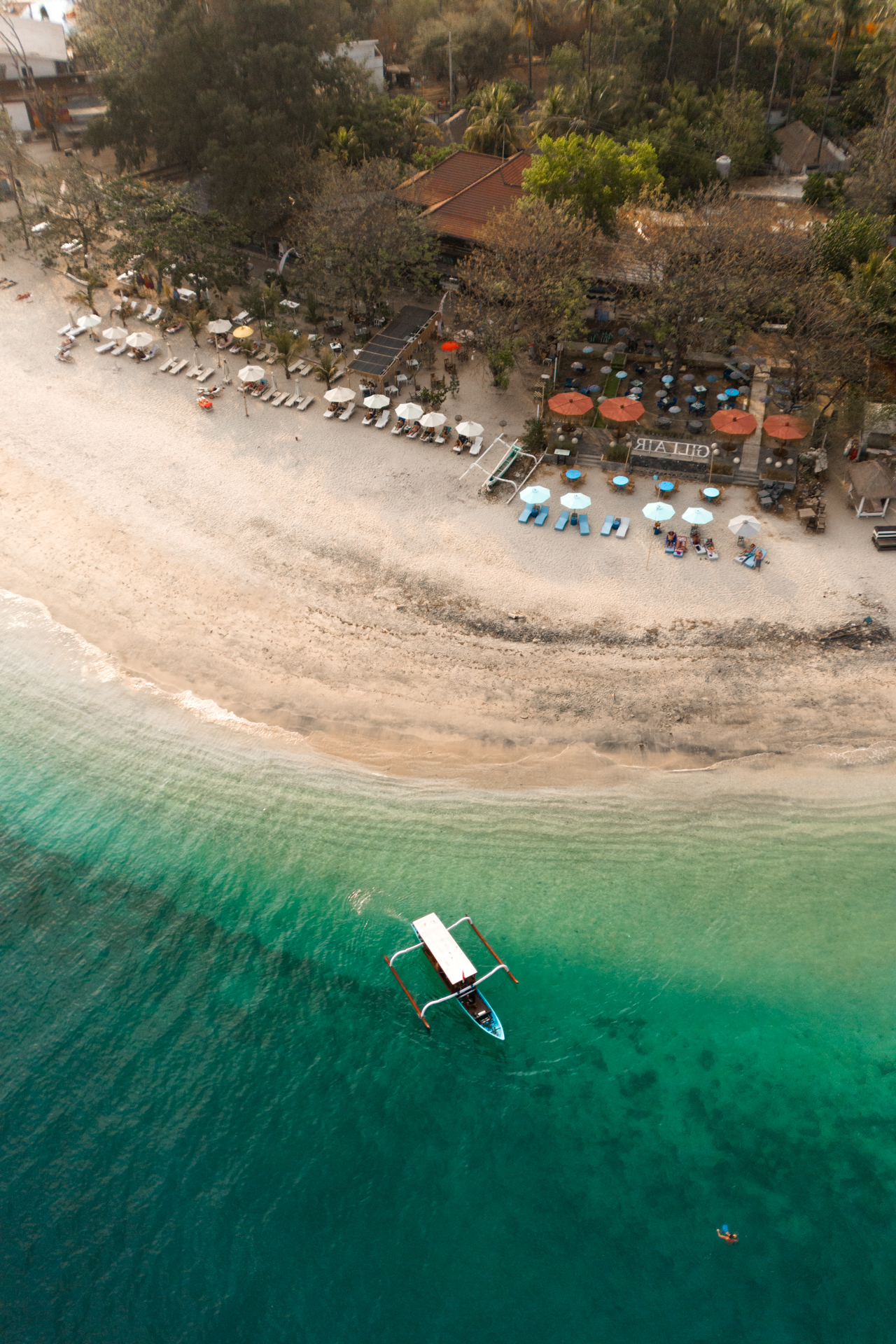 Drone shot of Gili Air coastline with traditional boat and clear shallow sea