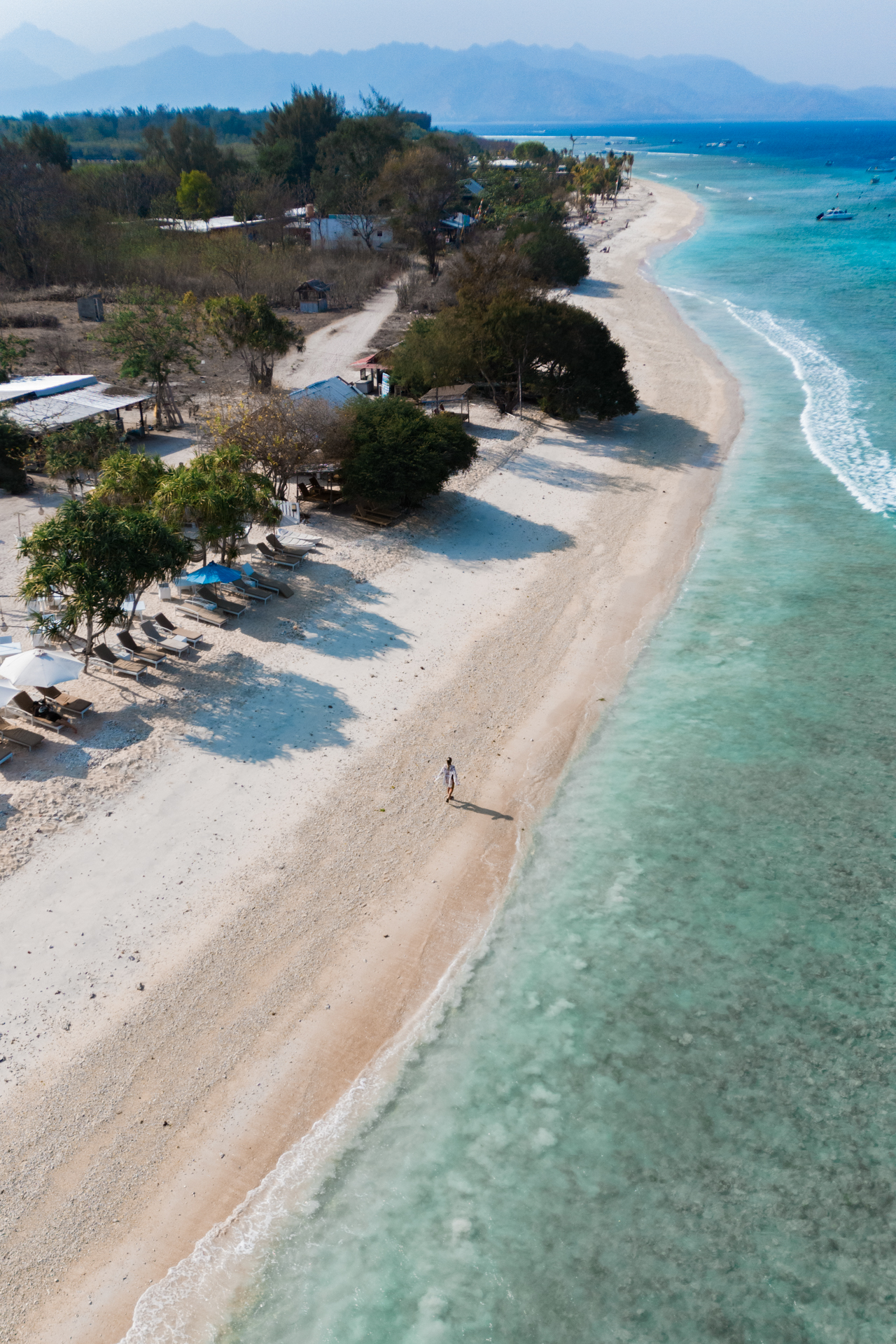 Peaceful beach on Gili Meno with crystal-clear water, white sand, and a lone person walking along the shoreline.