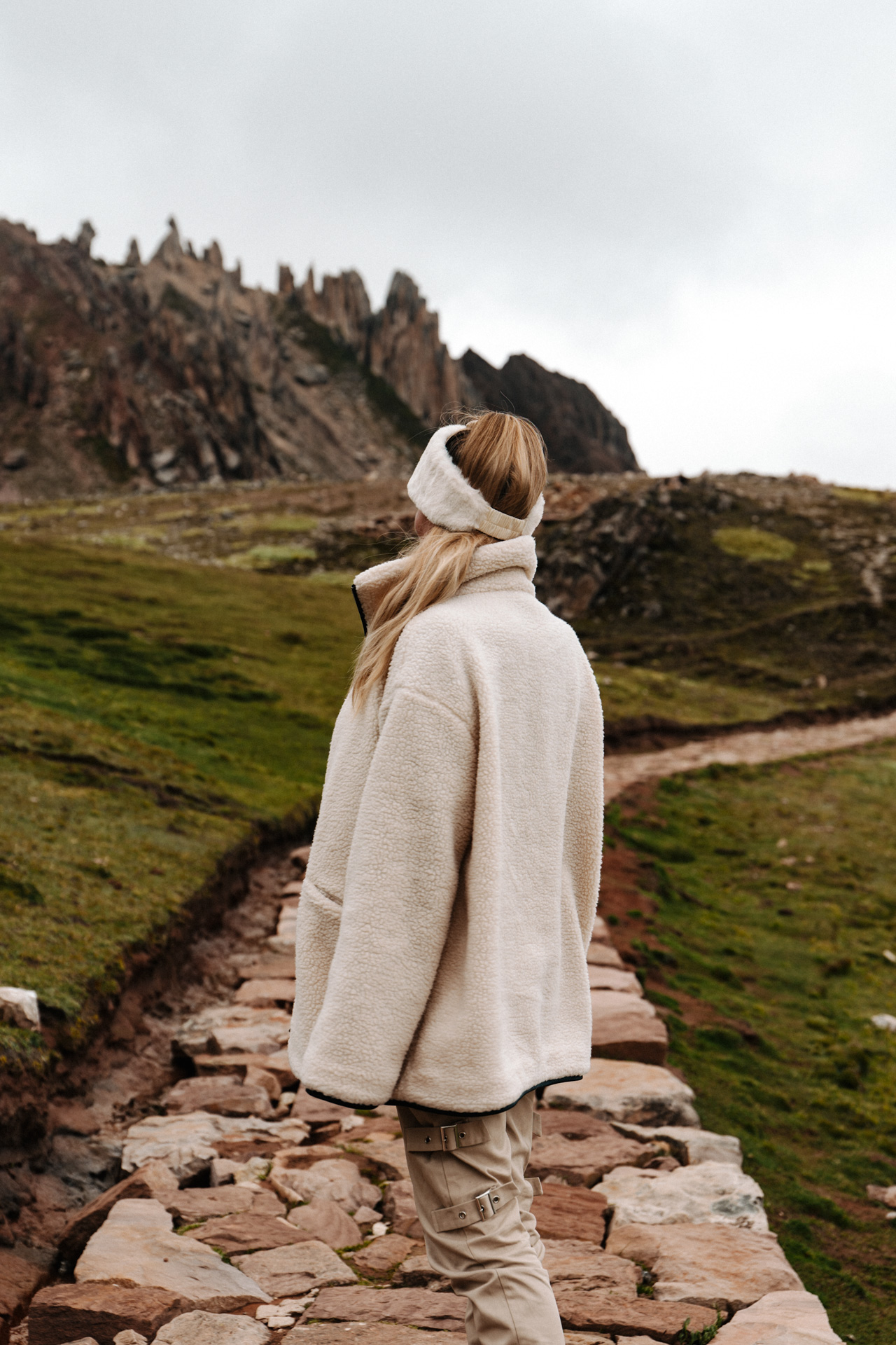 Woman walking along a stone path toward rocky peaks at Palccoyo, Peru