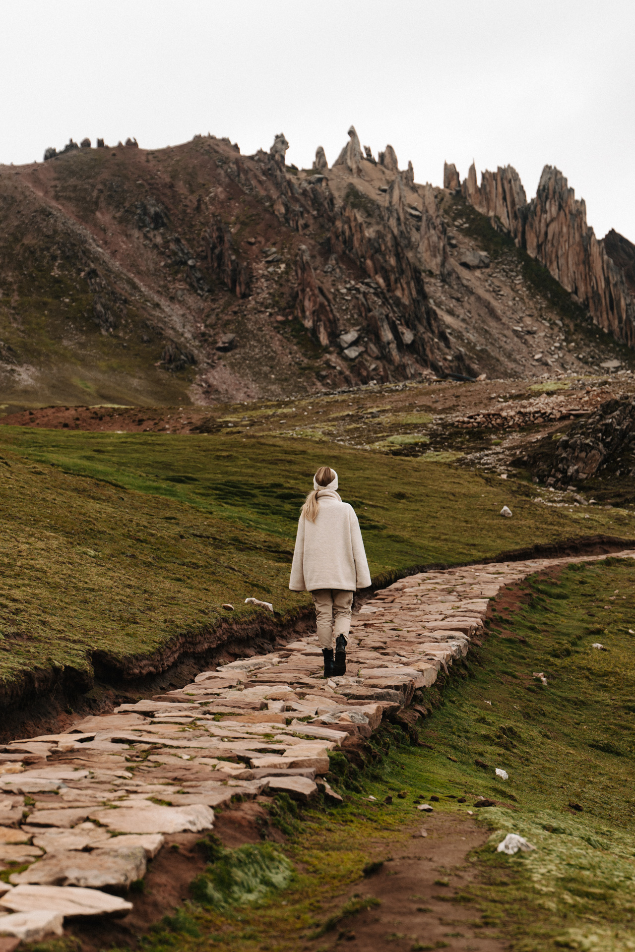 Hiker walking on ancient stone trail through green highlands near Palccoyo, Peru