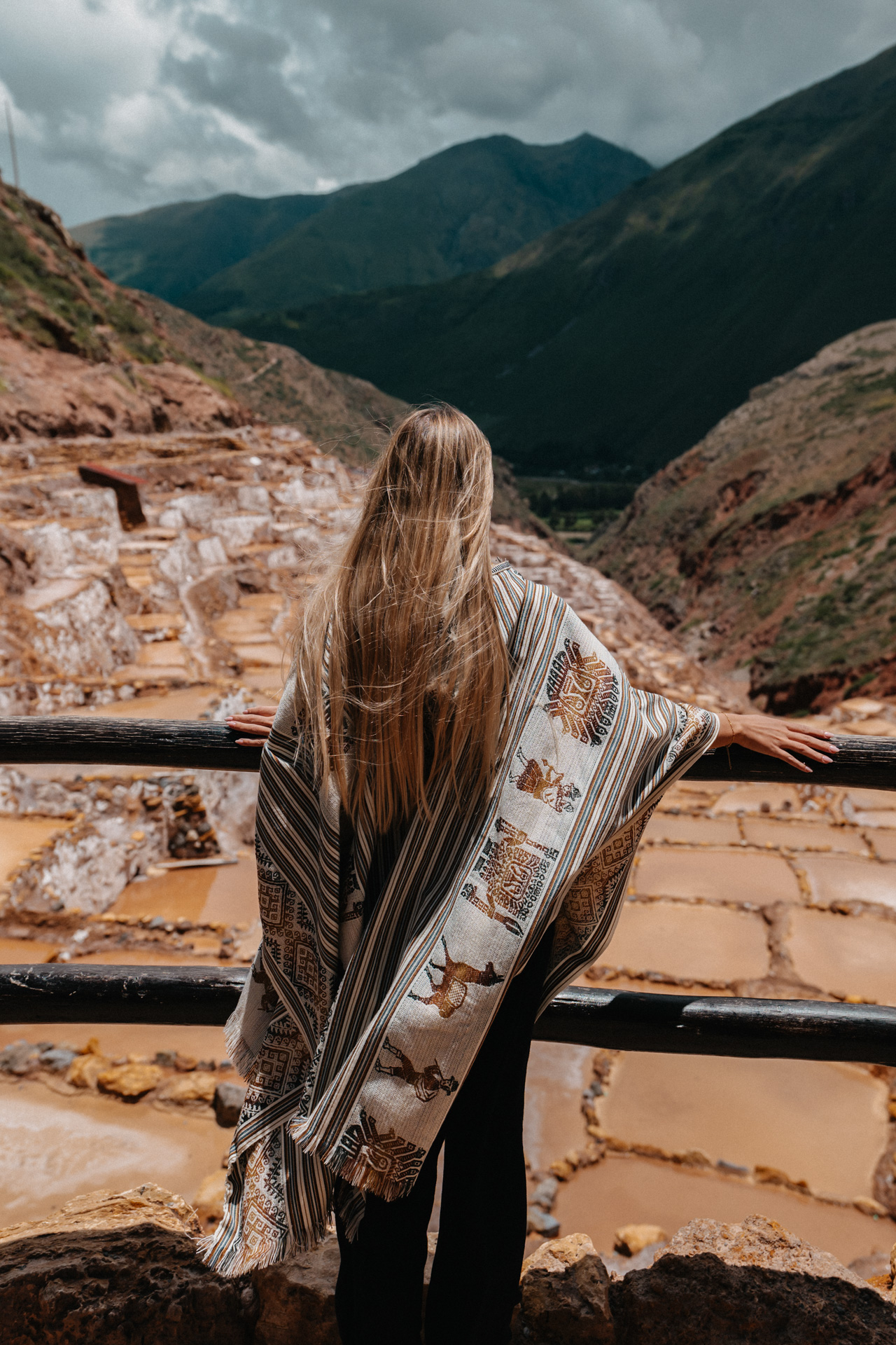 Traveler overlooking the salt pans of Maras with mountains in the Sacred Valley, Peru