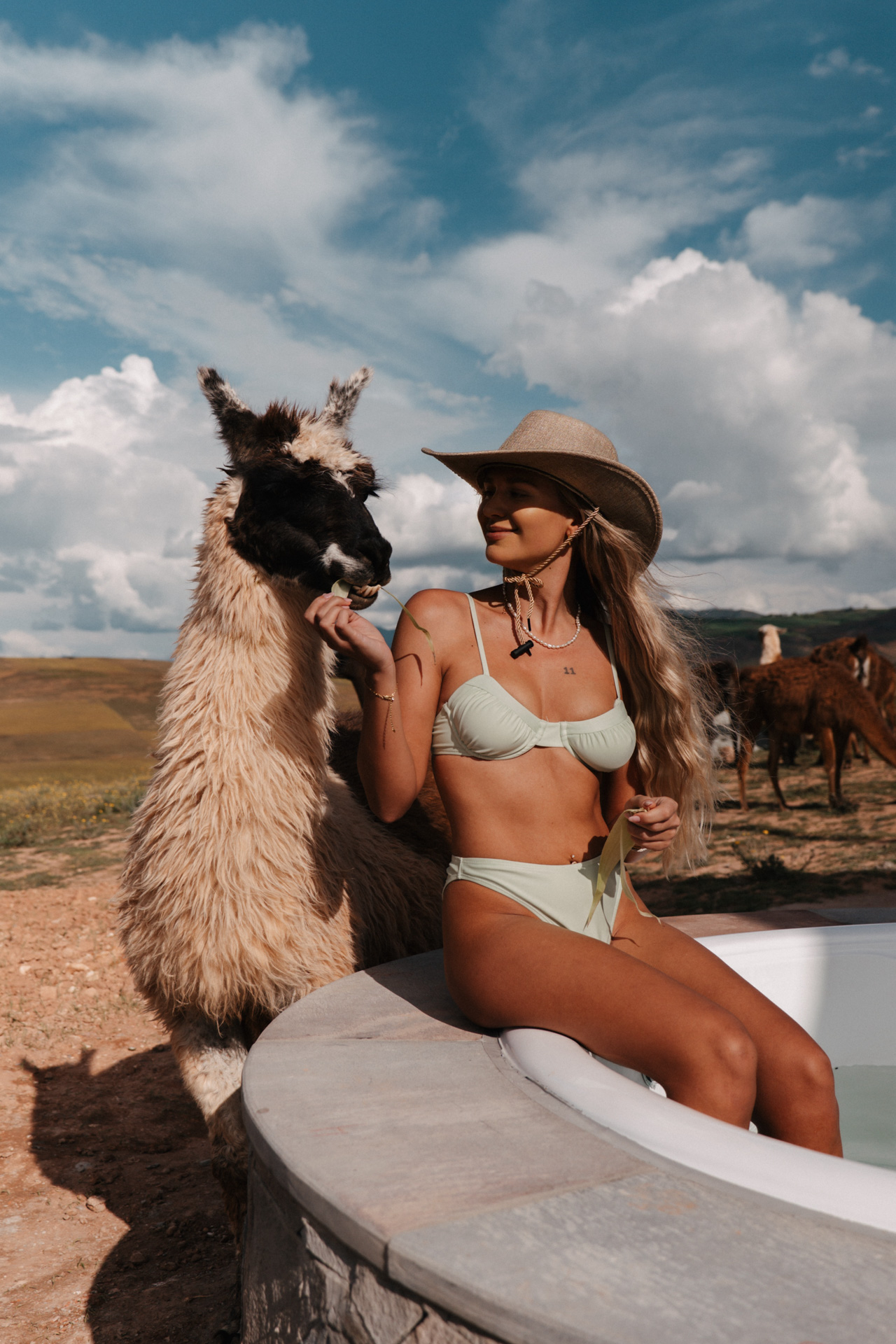 A woman relaxing in an outdoor hot tub while feeding a llama in Peru.