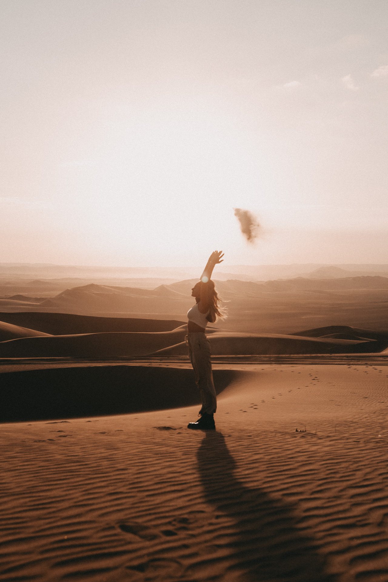 Woman standing on sand dunes at sunset in Huacachina Desert, Peru