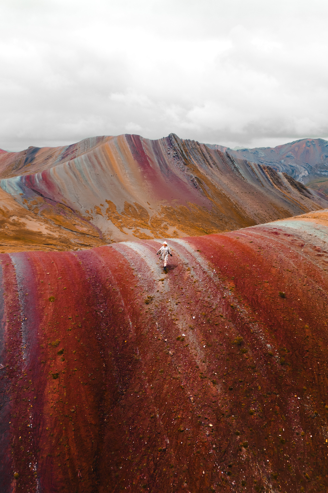 Hiker standing on colorful Rainbow Mountain ridges in Peru with dramatic landscape