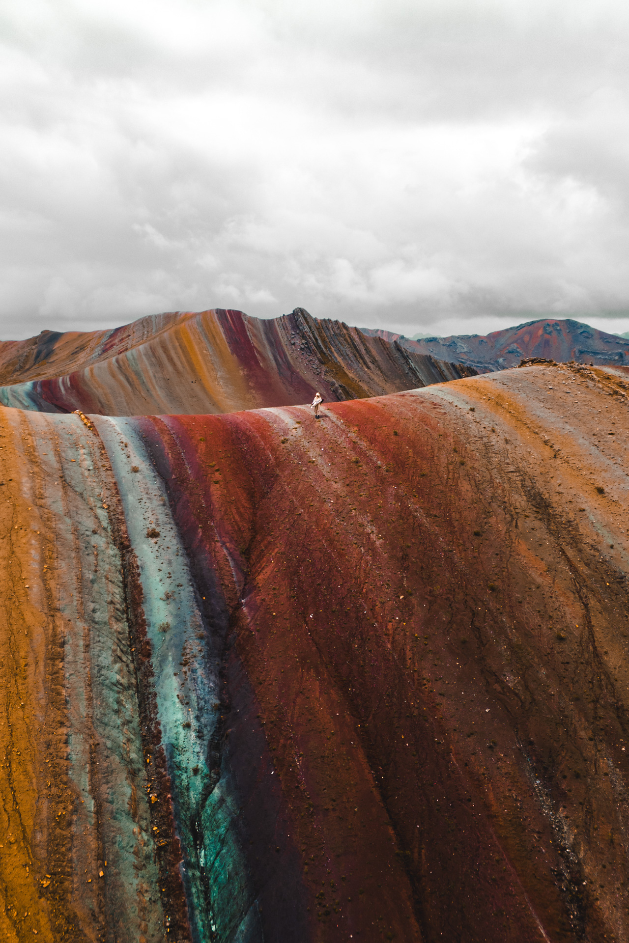 Hiker standing on colorful Rainbow Mountain ridges in Peru with dramatic landscape