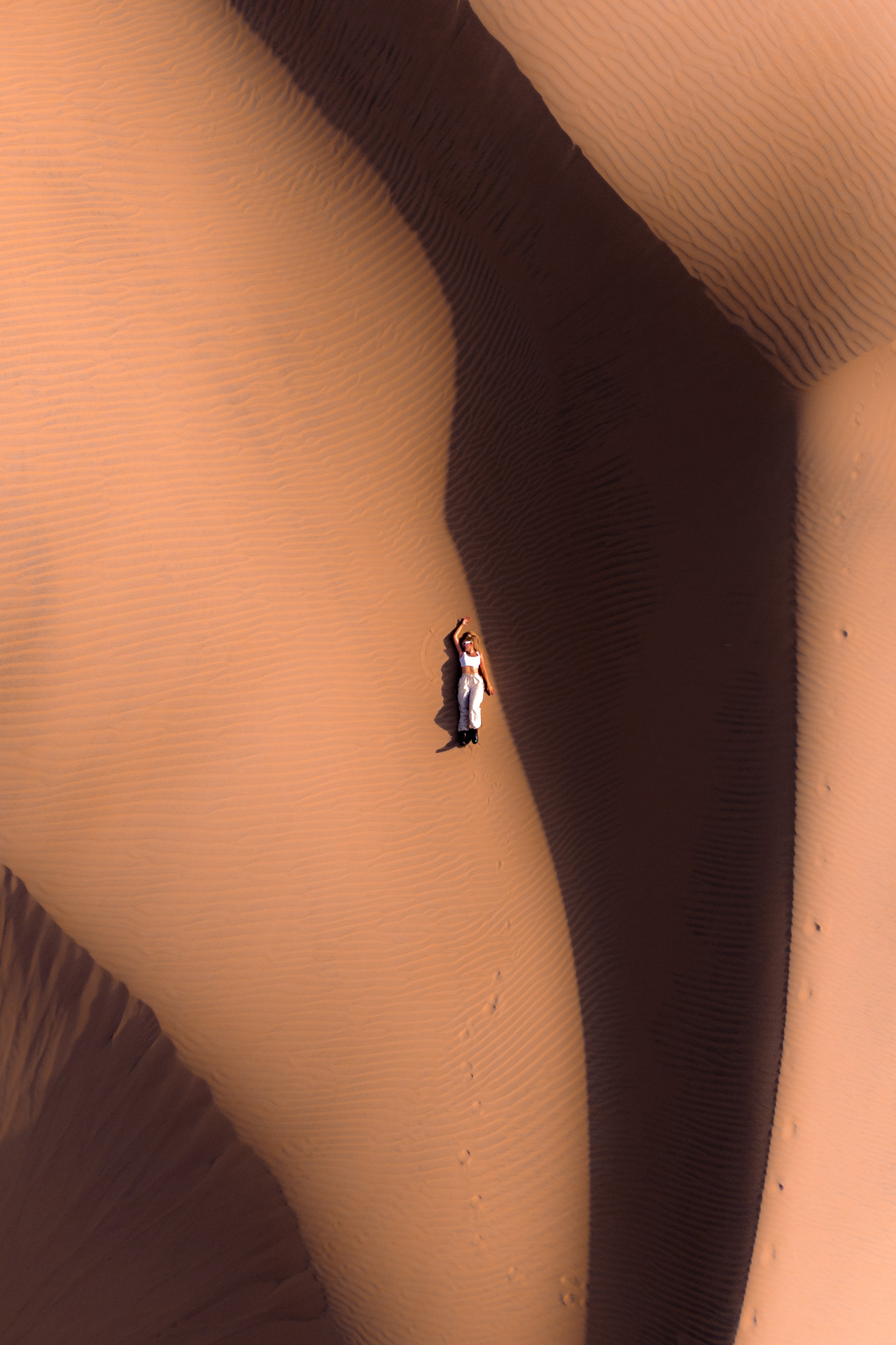 Aerial view of woman lying on sunlit sand dunes in Huacachina Desert, Peru