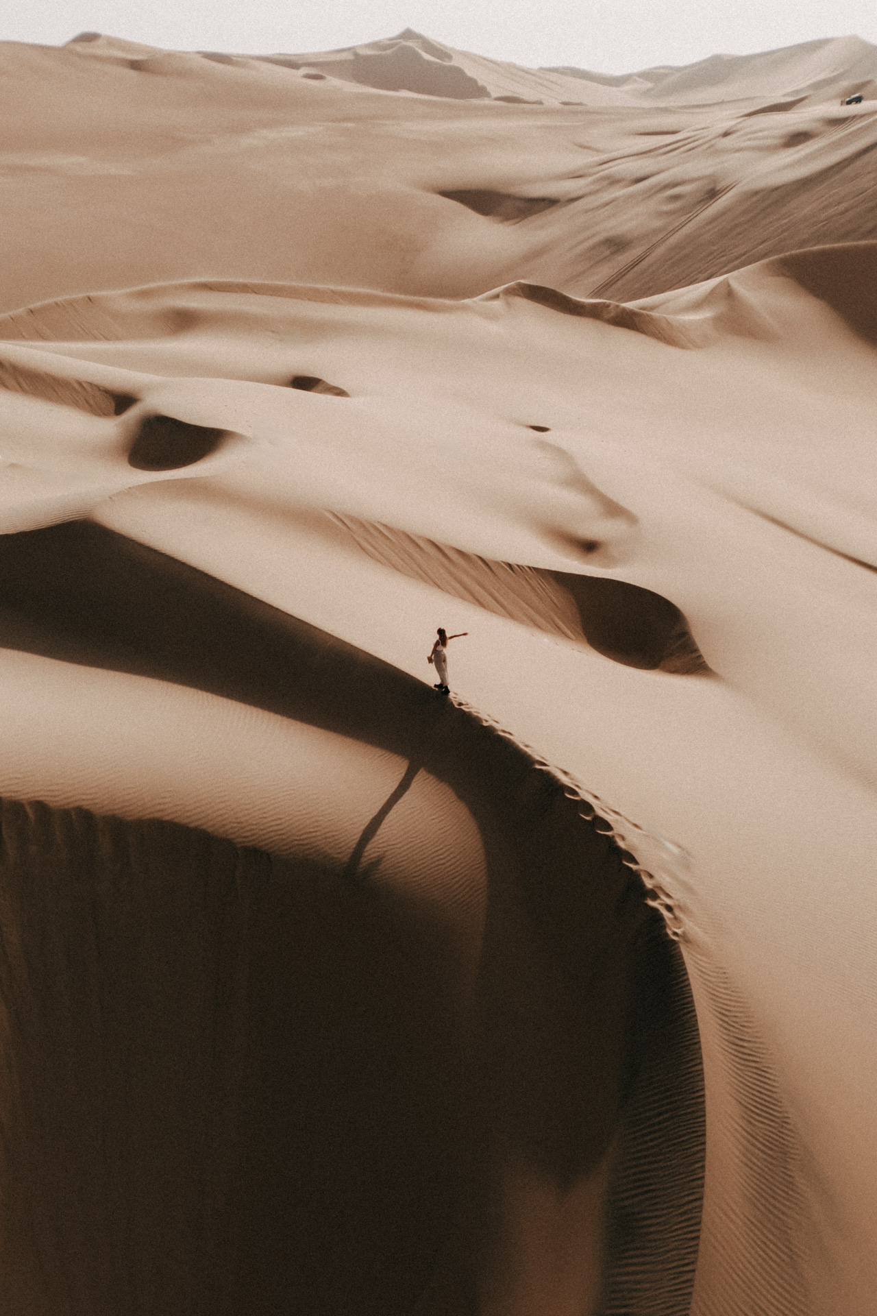 Aerial view of vast sand dunes with lone traveler in Huacachina, Peru