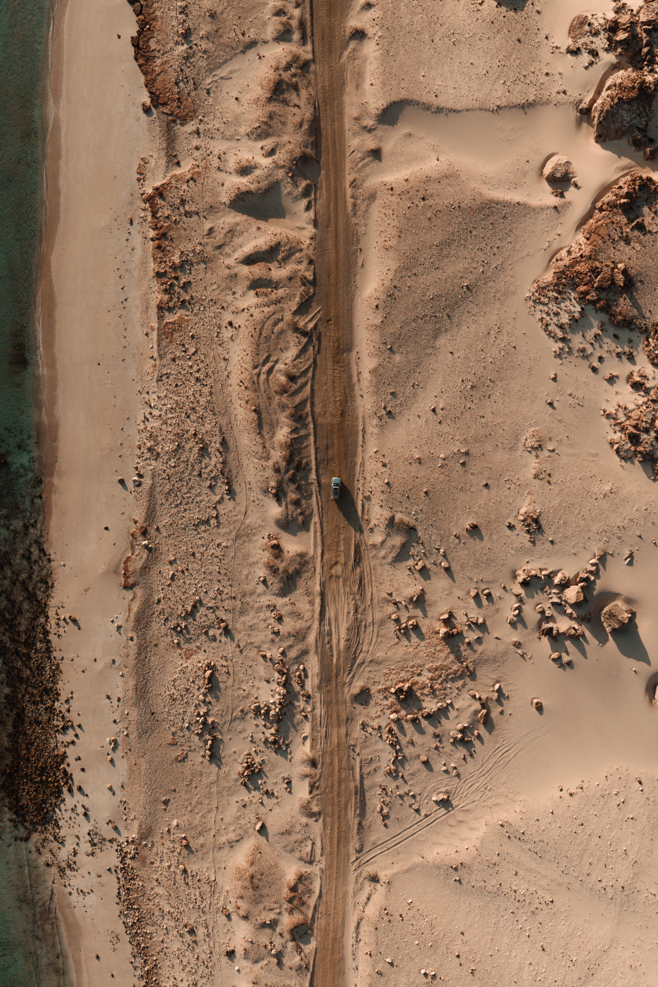 Aerial view of a 4x4 driving along a sandy coastal road on Socotra Island.