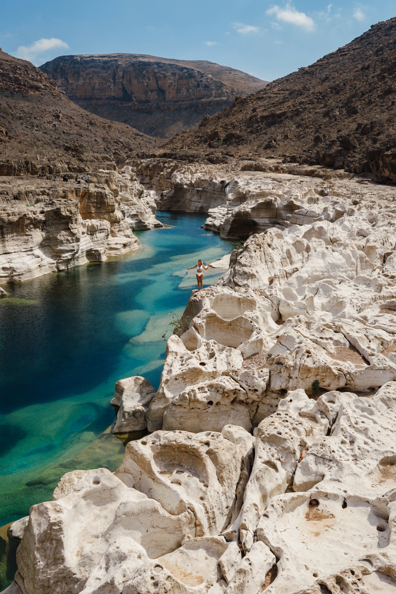Person standing on white cliffs above turquoise water in Wadi Kalissan