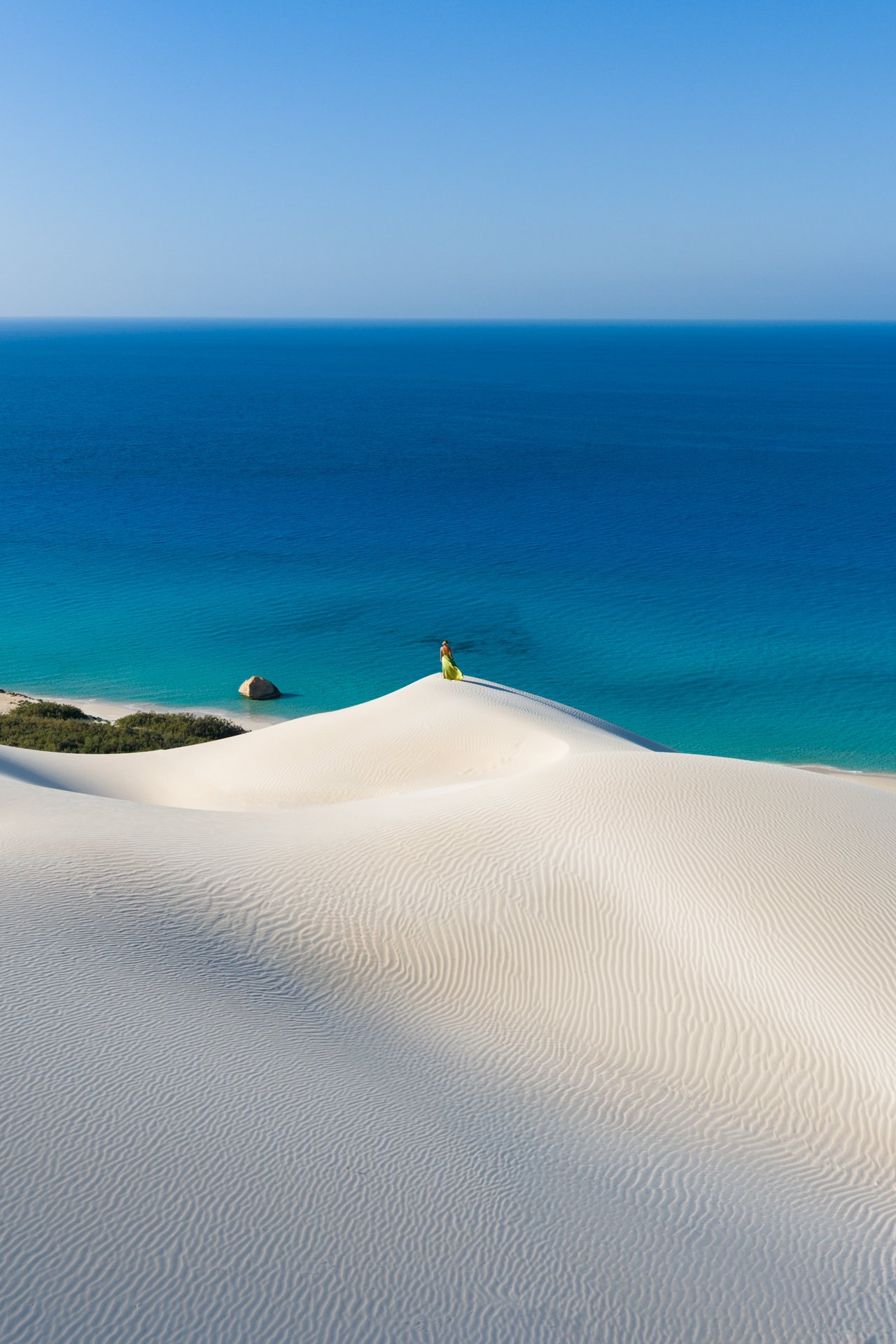 Person standing atop white sand dunes overlooking the deep blue sea at Arher Sand Dunes.
