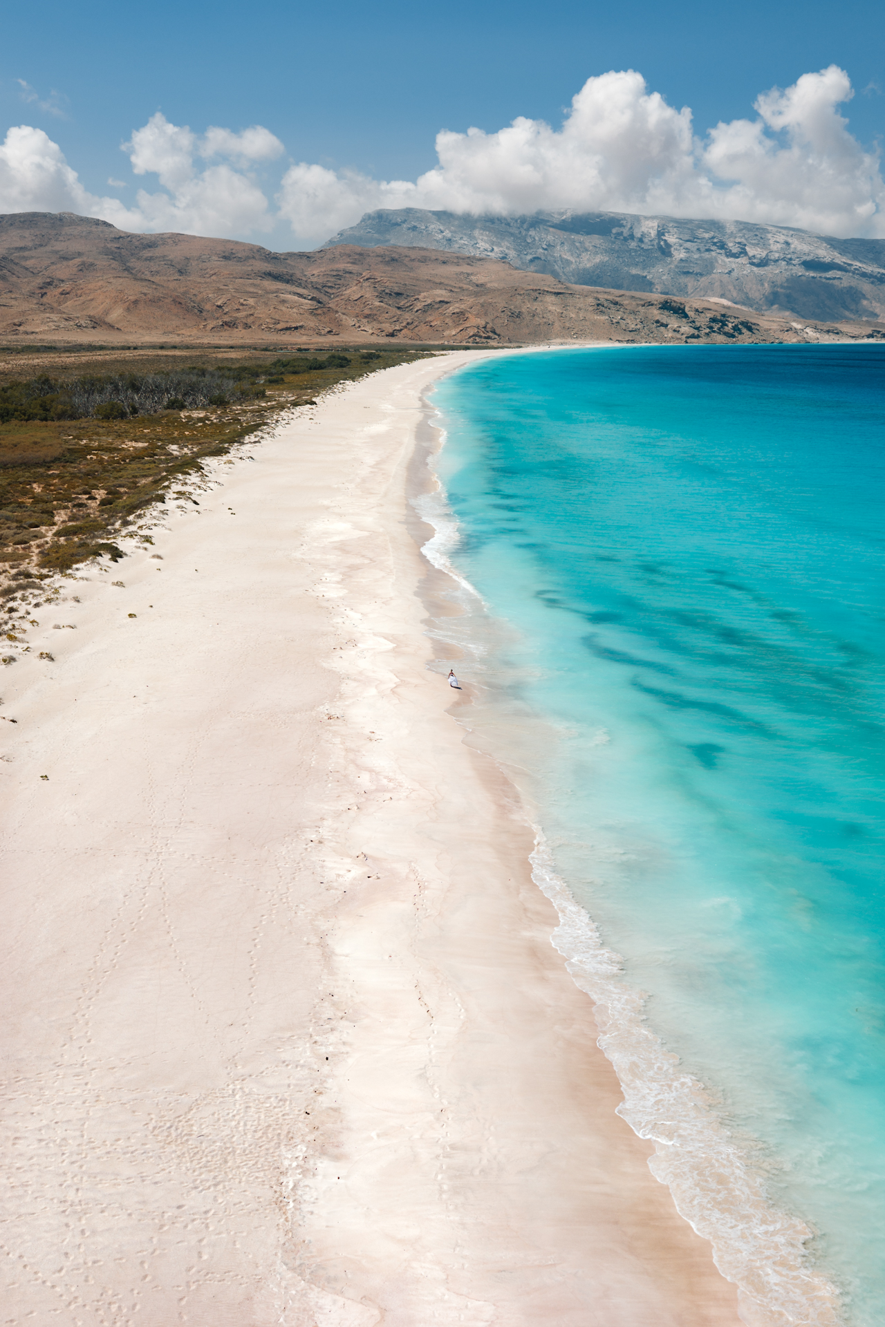 A person walking along the pristine white sand of Shoab Beach on Socotra Island.