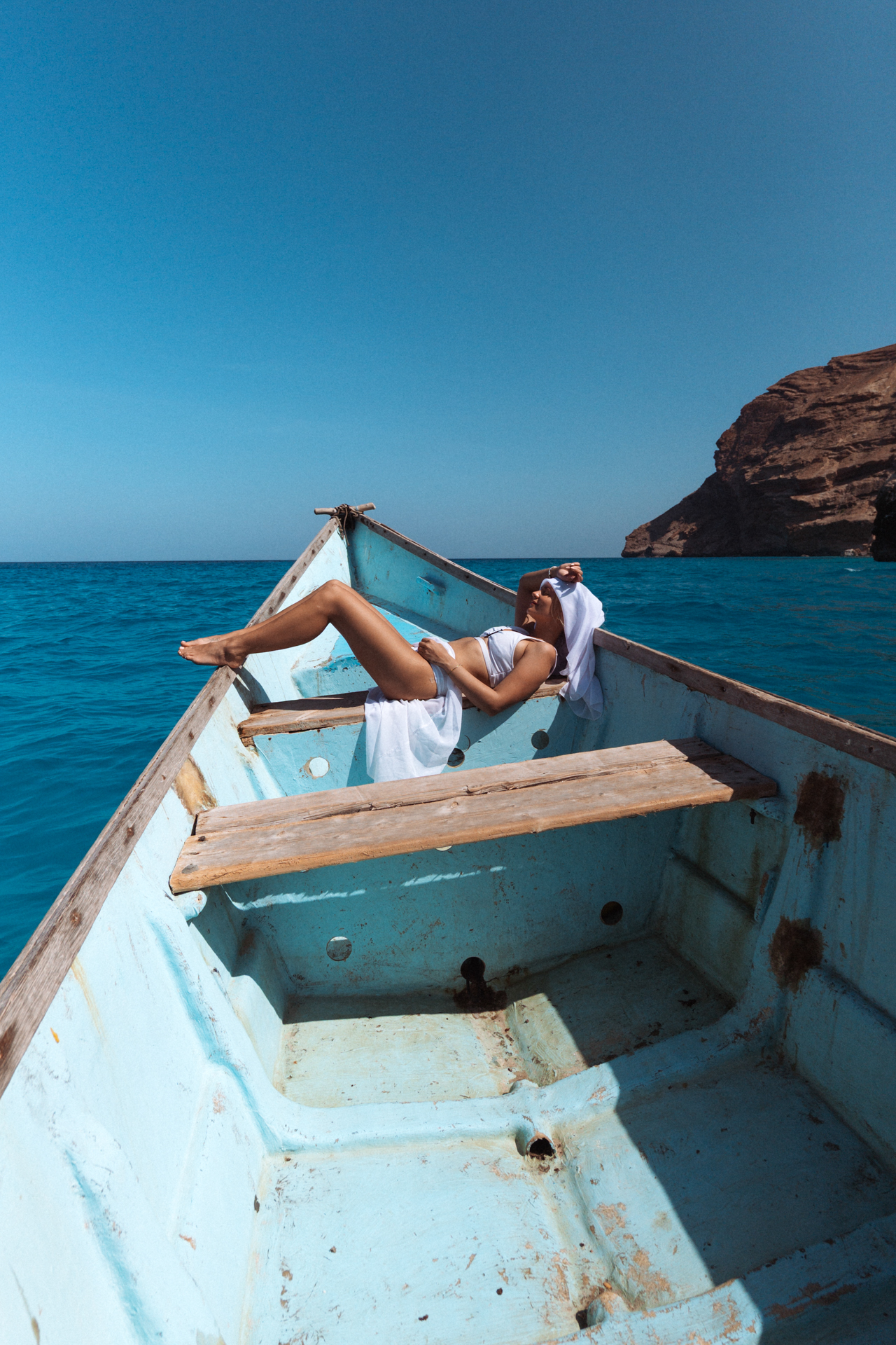 Woman relaxing on a wooden fishing boat near the cliffs of Shoab Bay on Socotra Island.
