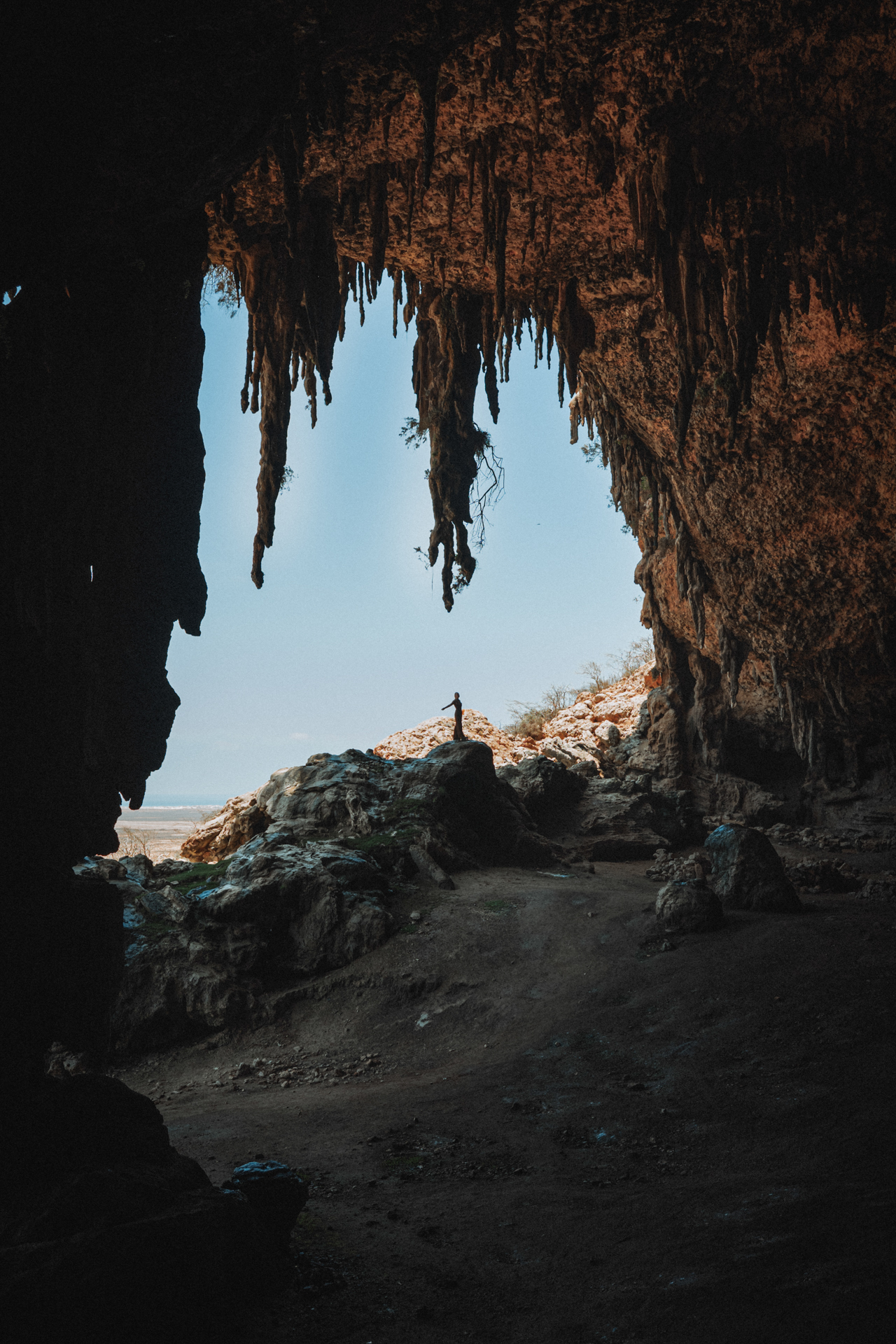 Inside Dagub Cave on Socotra Island, a person stands at the cave’s opening.