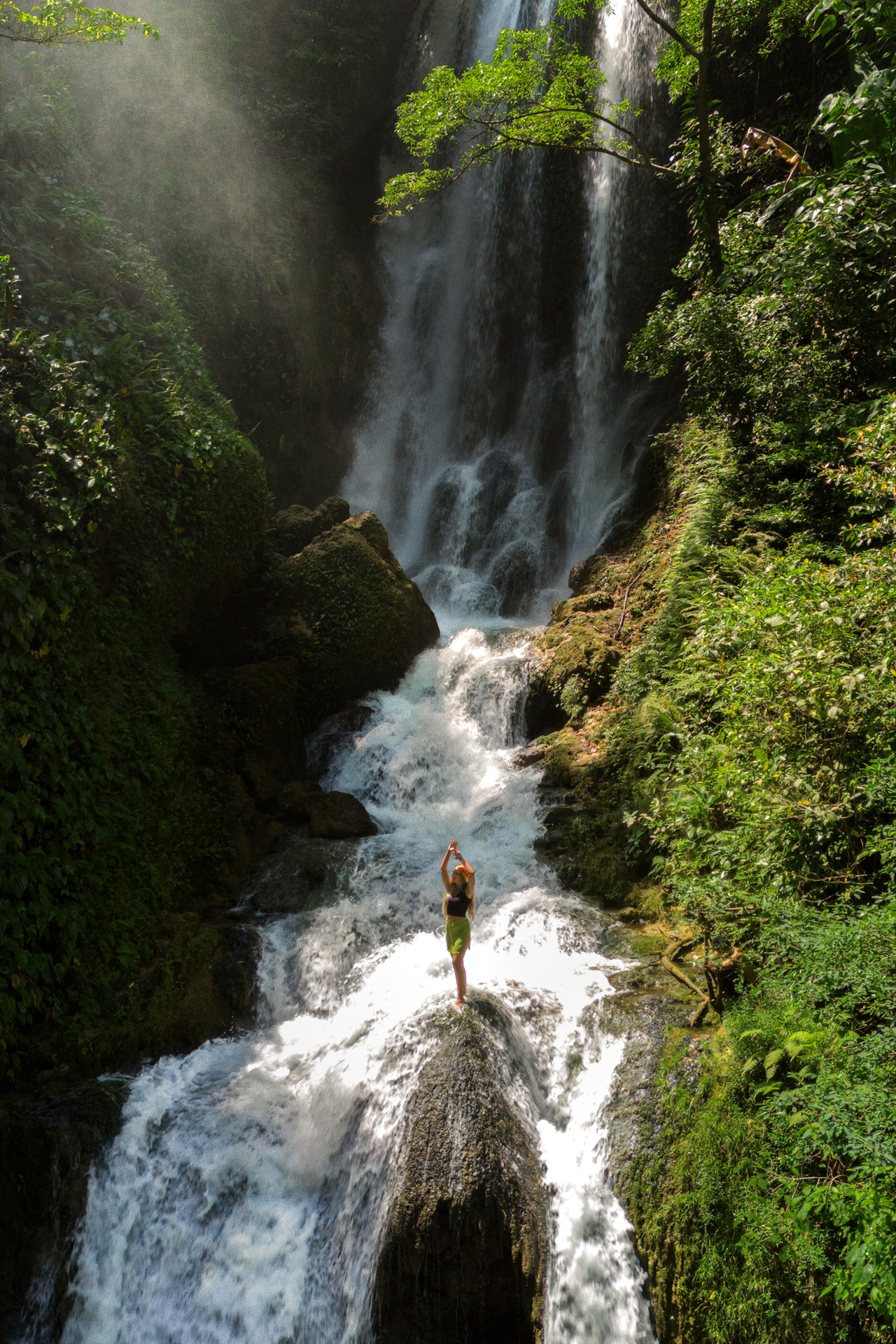Woman standing on rock beneath Lokomboro Waterfall, Sumba
