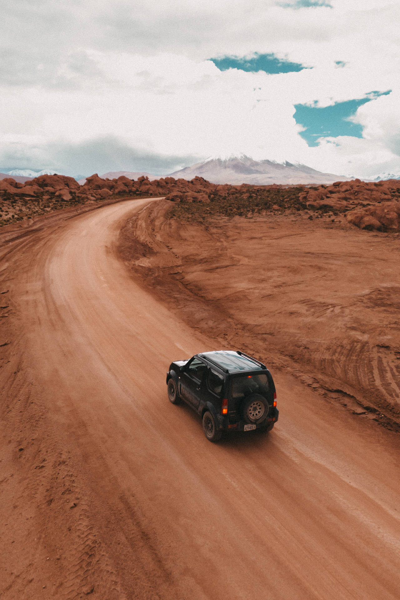 Off-road vehicle driving through the red desert landscape of Siloli Desert in Eduardo Avaroa National Reserve, Bolivia.