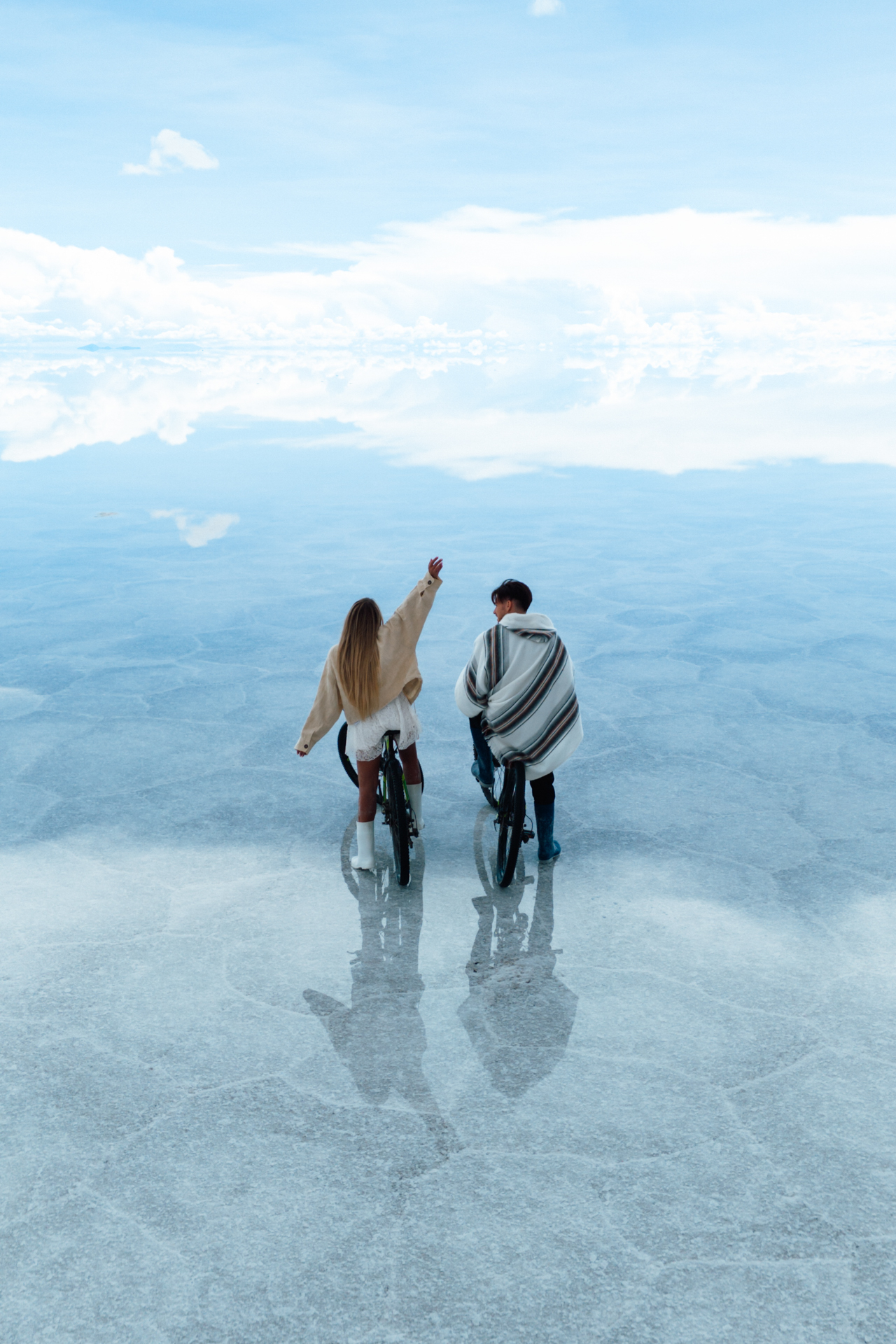 Couple riding bicycles across the mirror-like Salar de Uyuni salt flats, Bolivia.