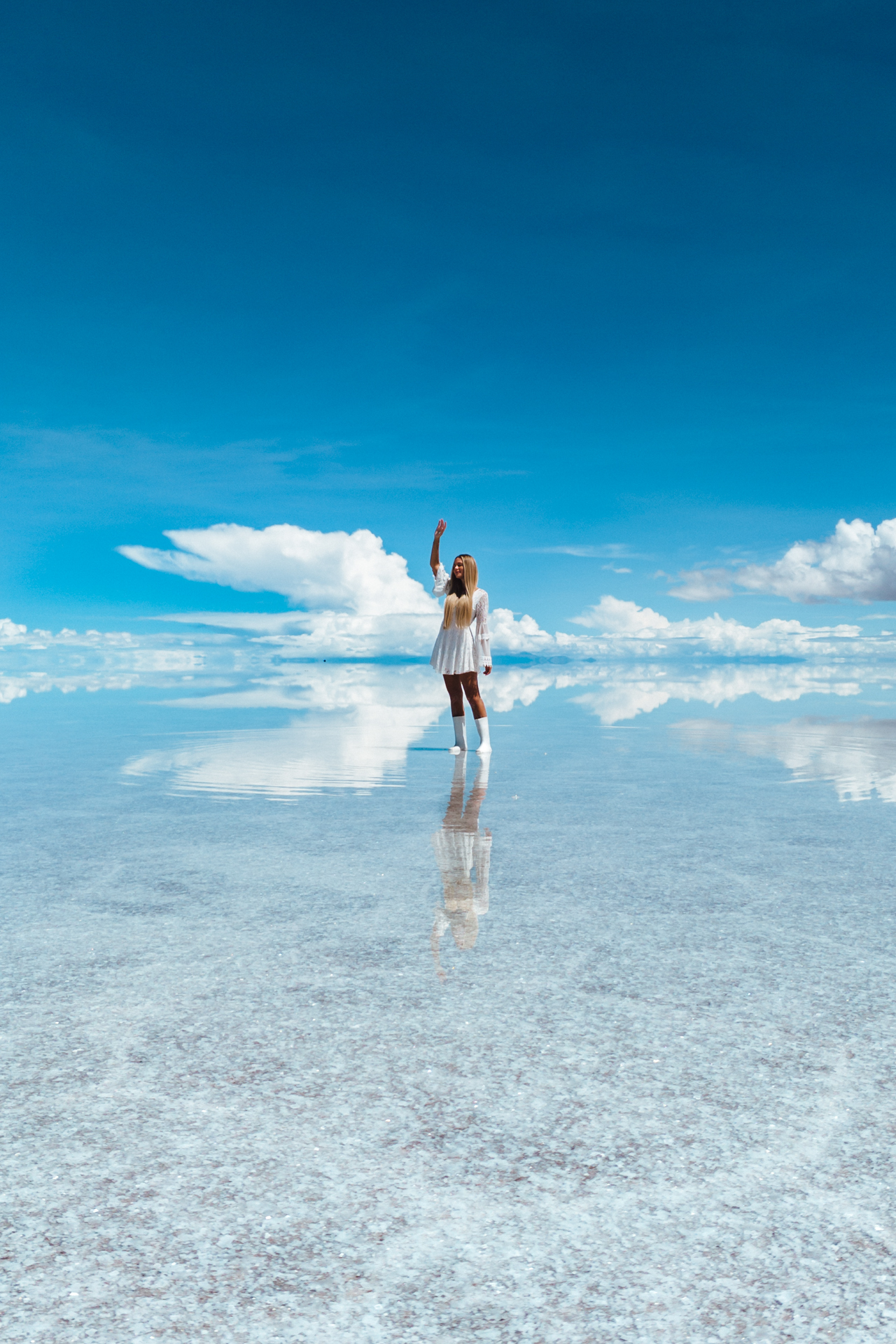 Woman standing on the reflective surface of Salar de Uyuni salt flats under a bright blue sky, Bolivia.