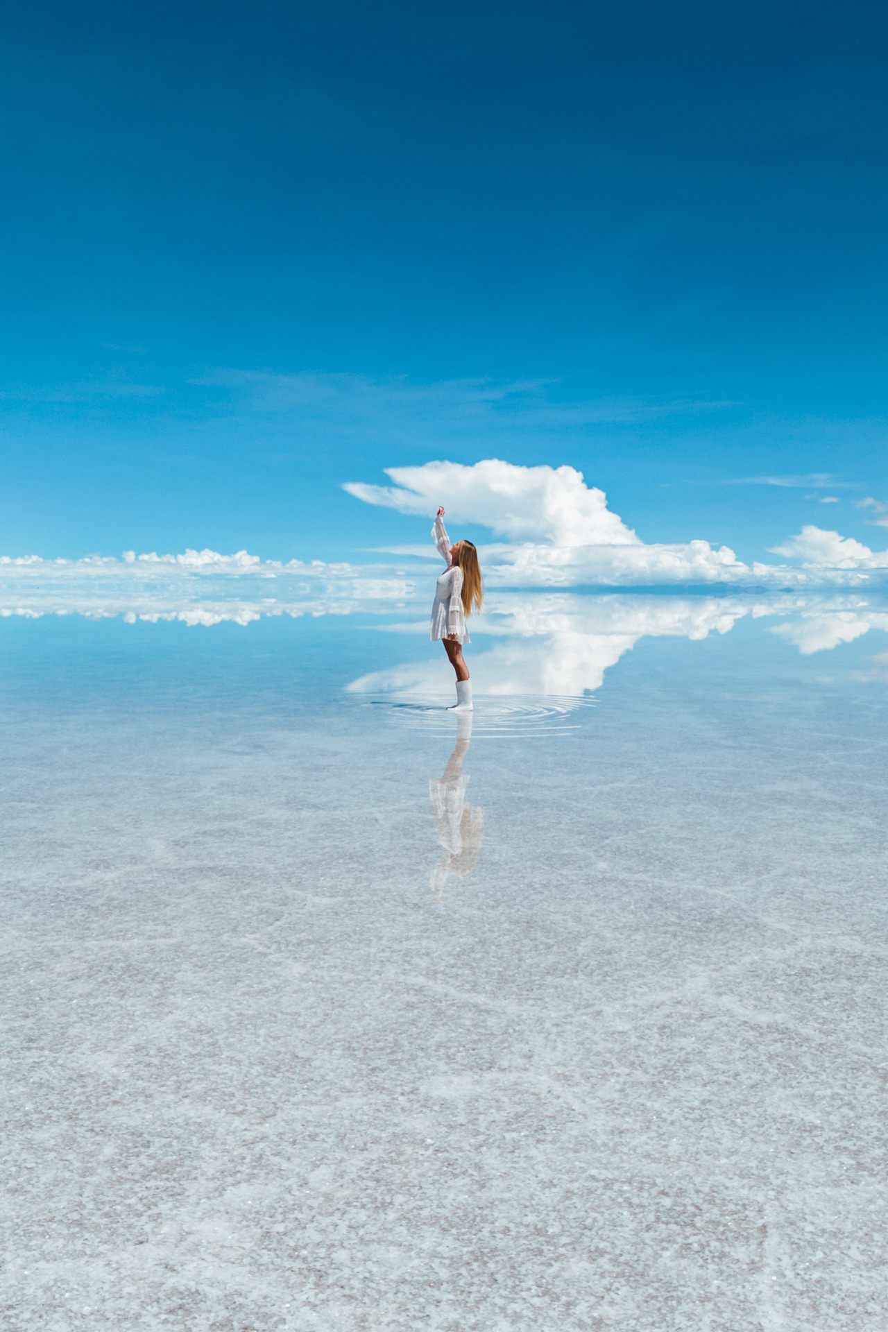 Woman standing on the reflective surface of Salar de Uyuni salt flats under a bright blue sky, Bolivia.