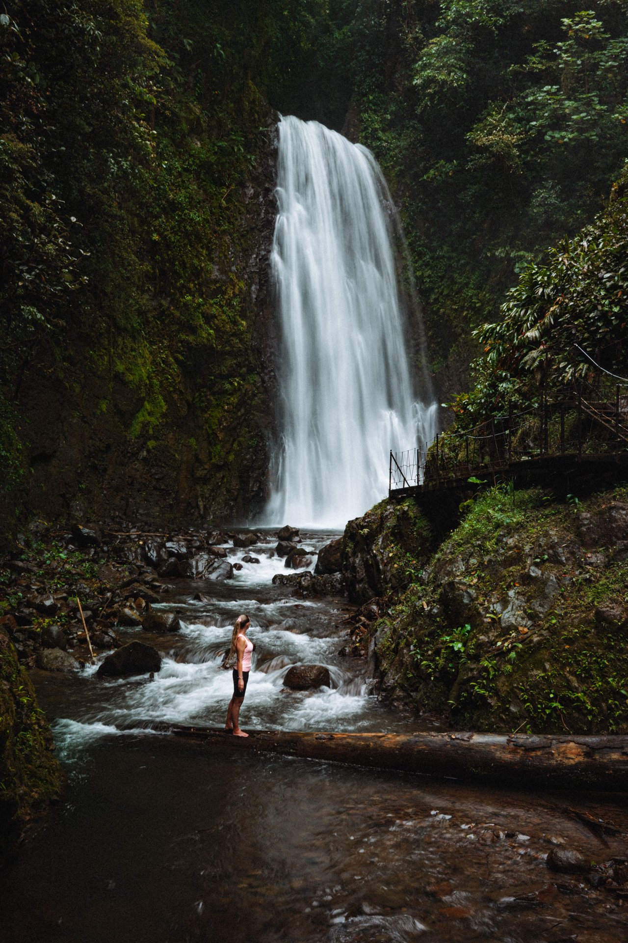 Woman standing on a log in front of EL Tigre waterfall in Monteverde Costa Rica