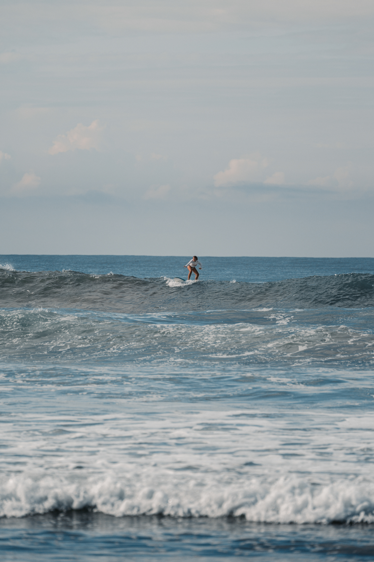 Surfer riding a wave in Santa Teresa, Costa Rica with blue ocean and gentle waves