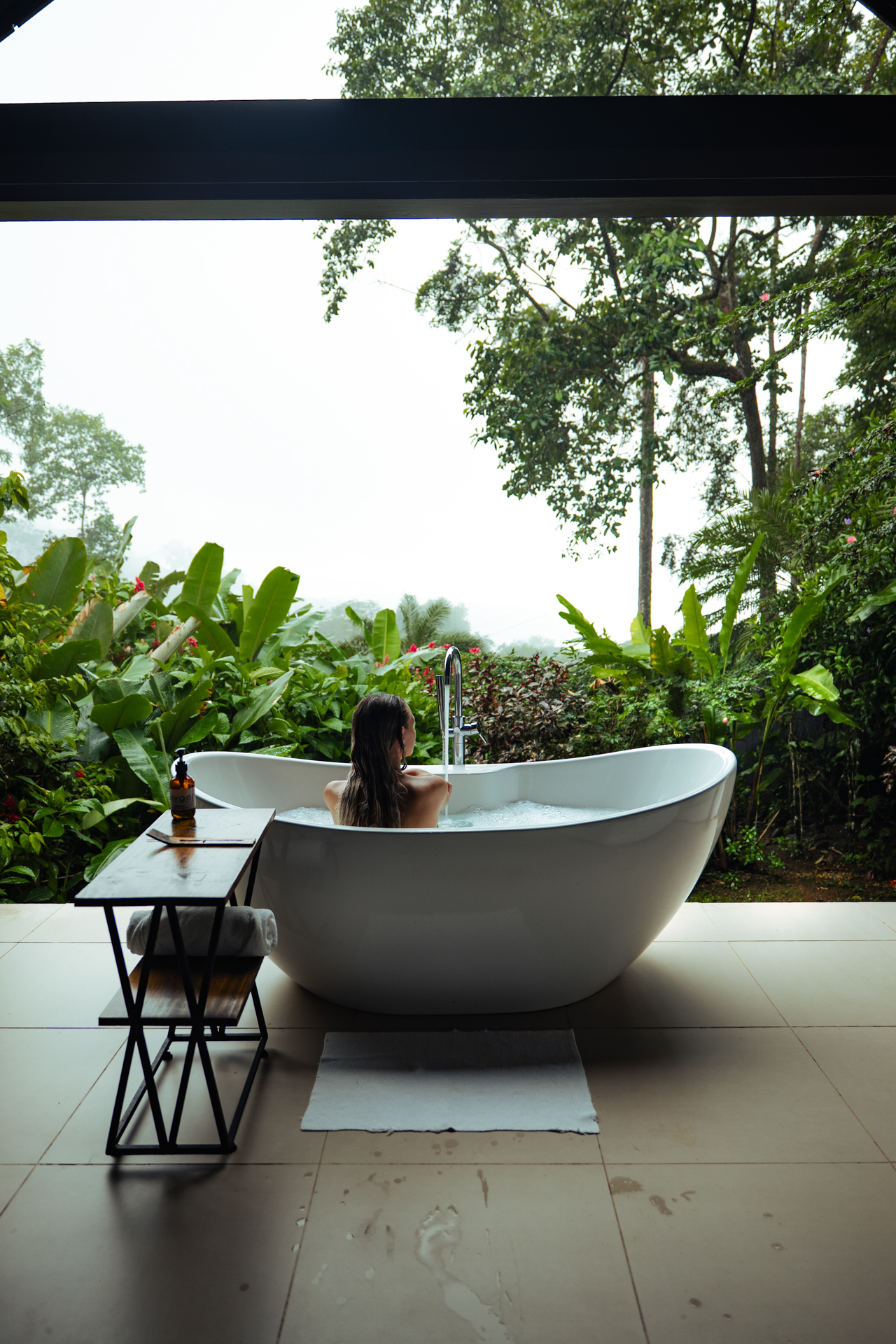 Outdoor bathtub in Costa Rica jungle with woman relaxing and tropical rainforest view.