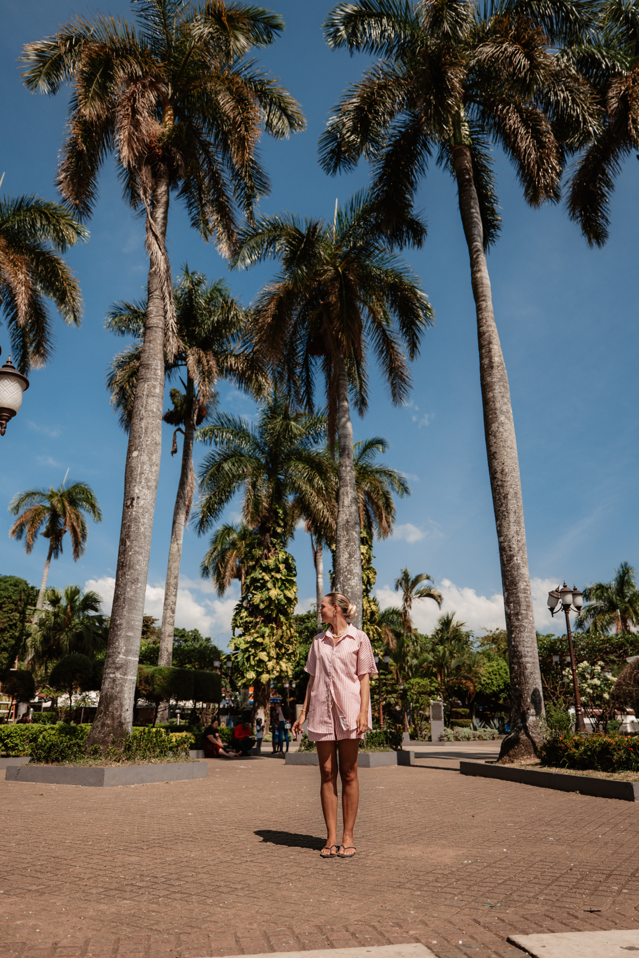 Traveler standing beneath tall palm trees in the central plaza of Nahuizalco on the Ruta de las Flores in El Salvador