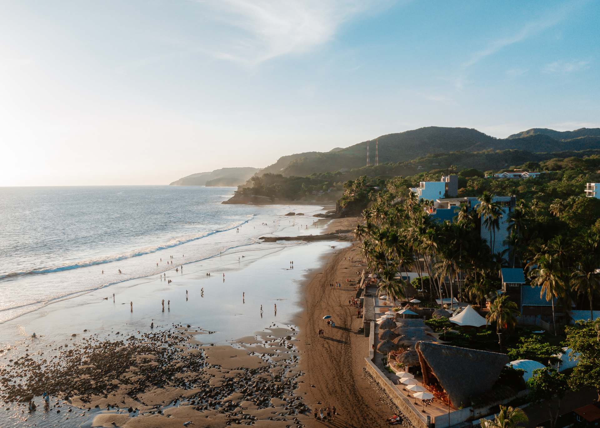 Aerial view of a tropical beach in El Salvador, El Zonte with surfers, palm trees, and coastline at sunset