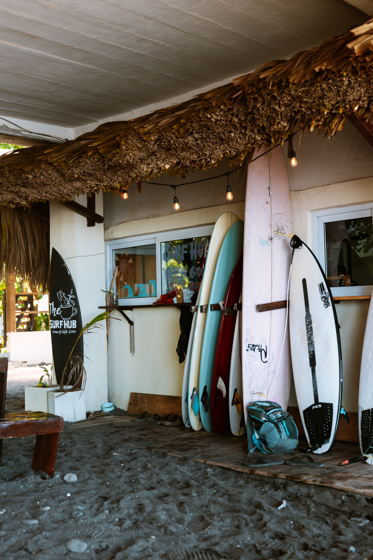Colorful surfboards outside a small beach surf shop with thatched roof and warm light in El Zonte, El Salvador.