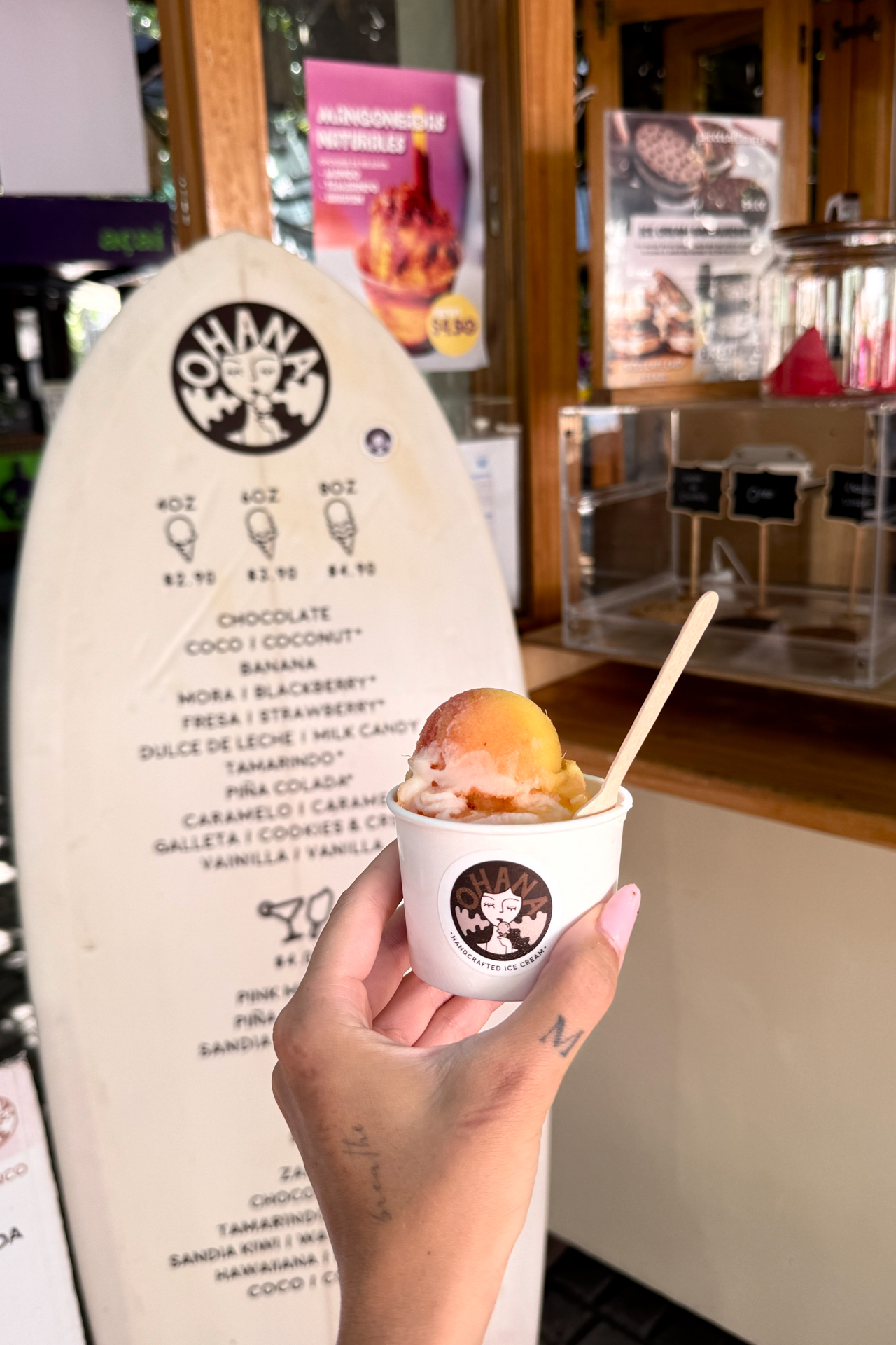Hand holding ice cream from Ohana shop in El Tunco with surfboard-style menu behind